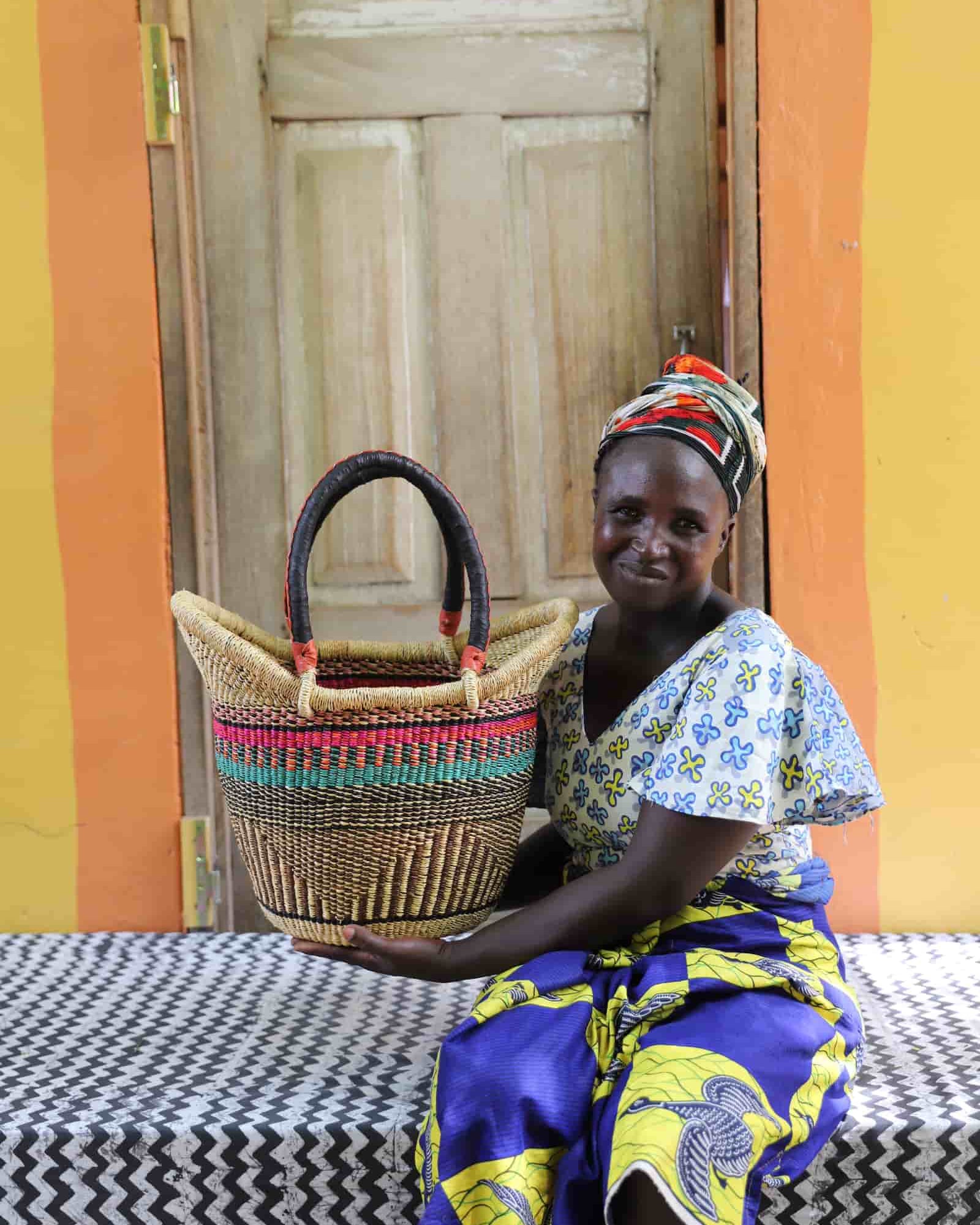 Woman holding Nyariga shopping basket in natural straw with pink and teal stripe detail