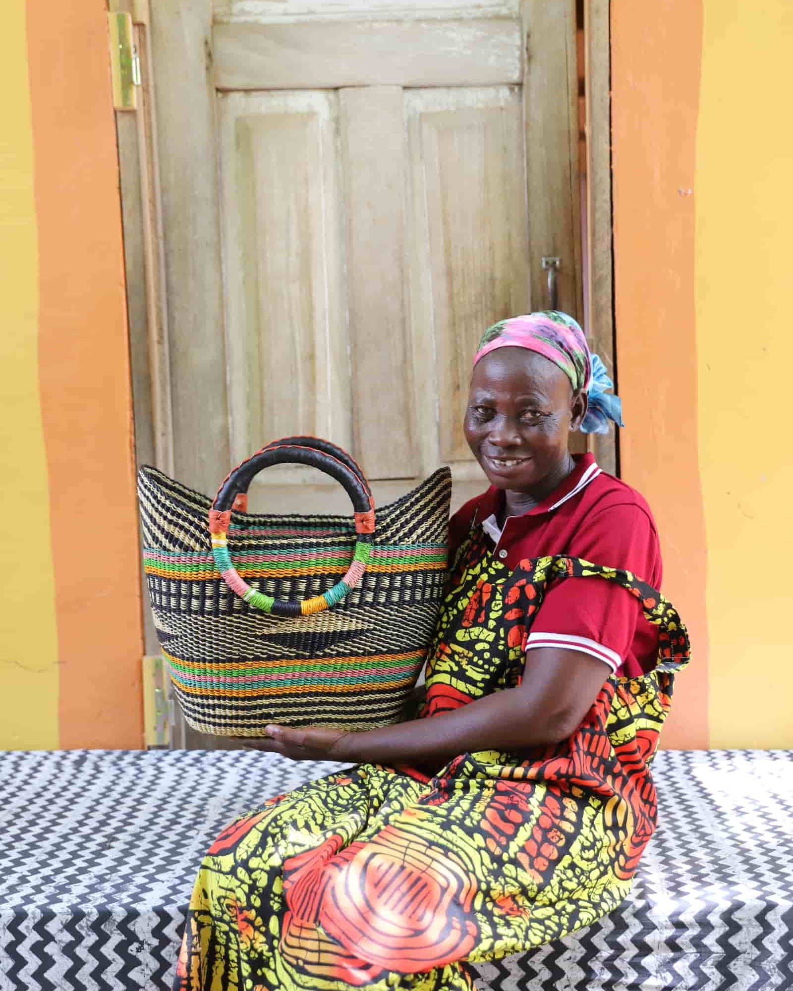 Woman in yellow and red African print dress holding a woven black and natural striped beach bag