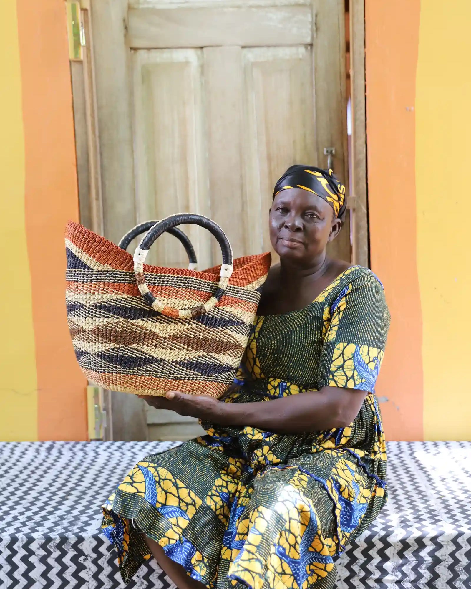 Woman in gold African print dress holding a woven beach bag in terracotta and brown diagonal stripes