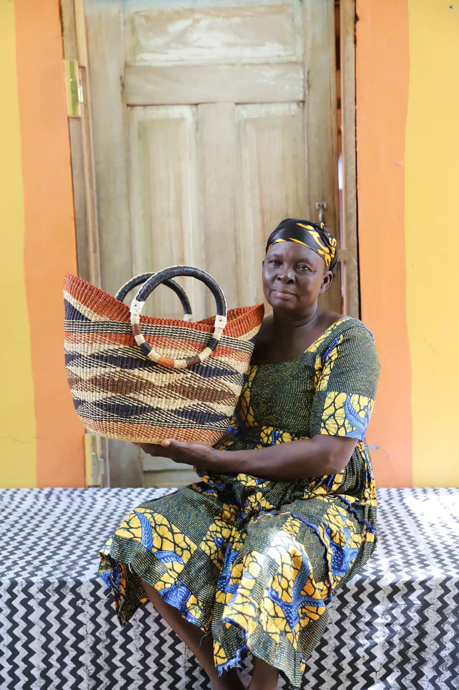 Woman in gold African print dress holding a woven beach bag in terracotta and brown diagonal stripes