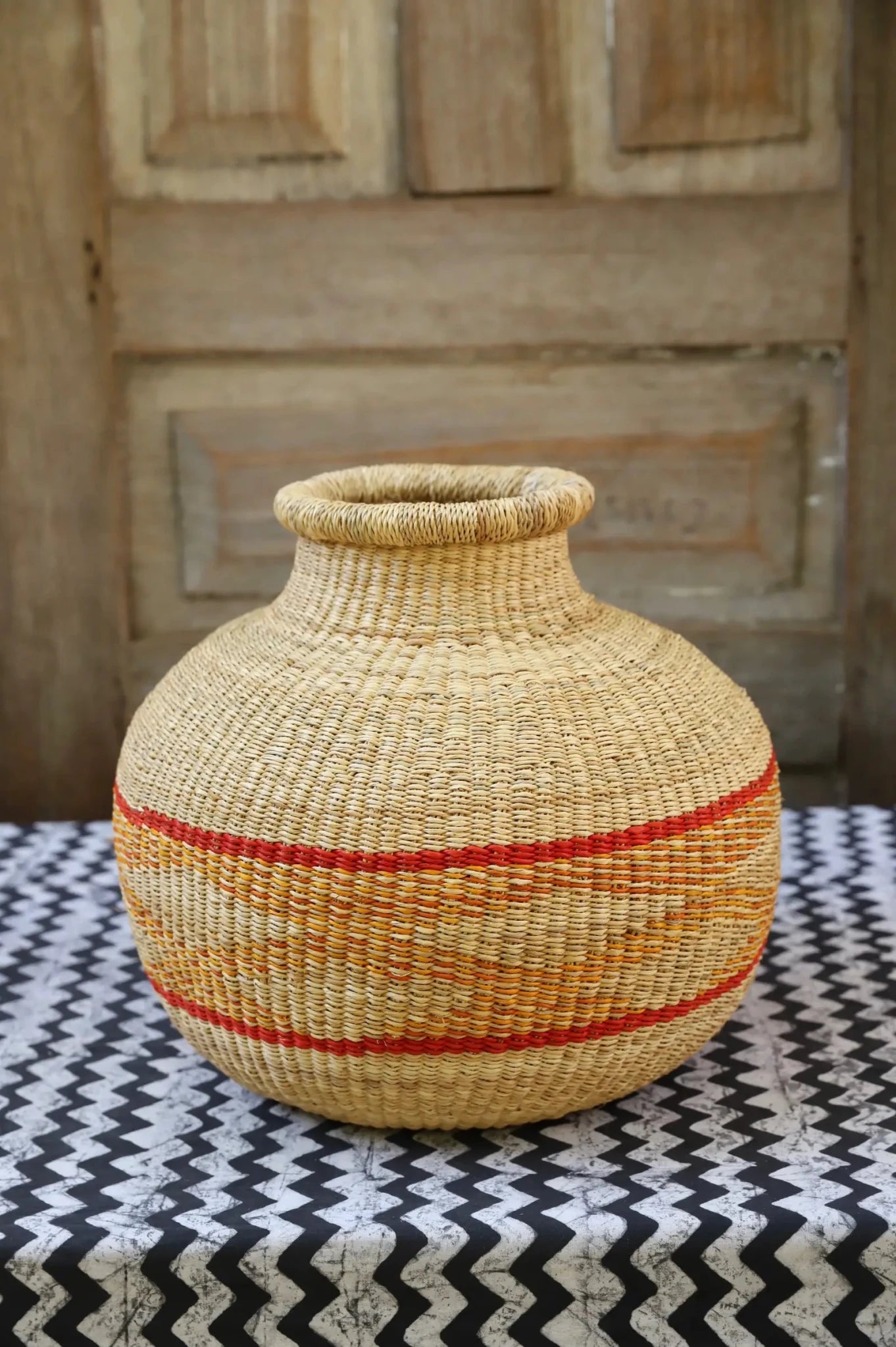 Decorative handwoven basket with colorful patterns on a black and white cloth against a wooden door.