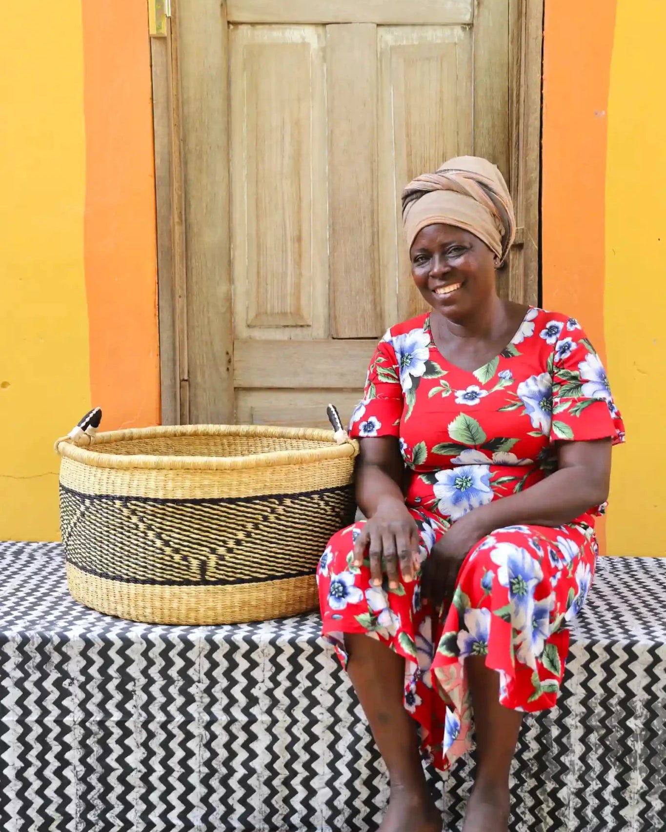 Woven Tub (Large) with woman weaver handwoven in Ghana sitting on black and white cloth and wooden door in background