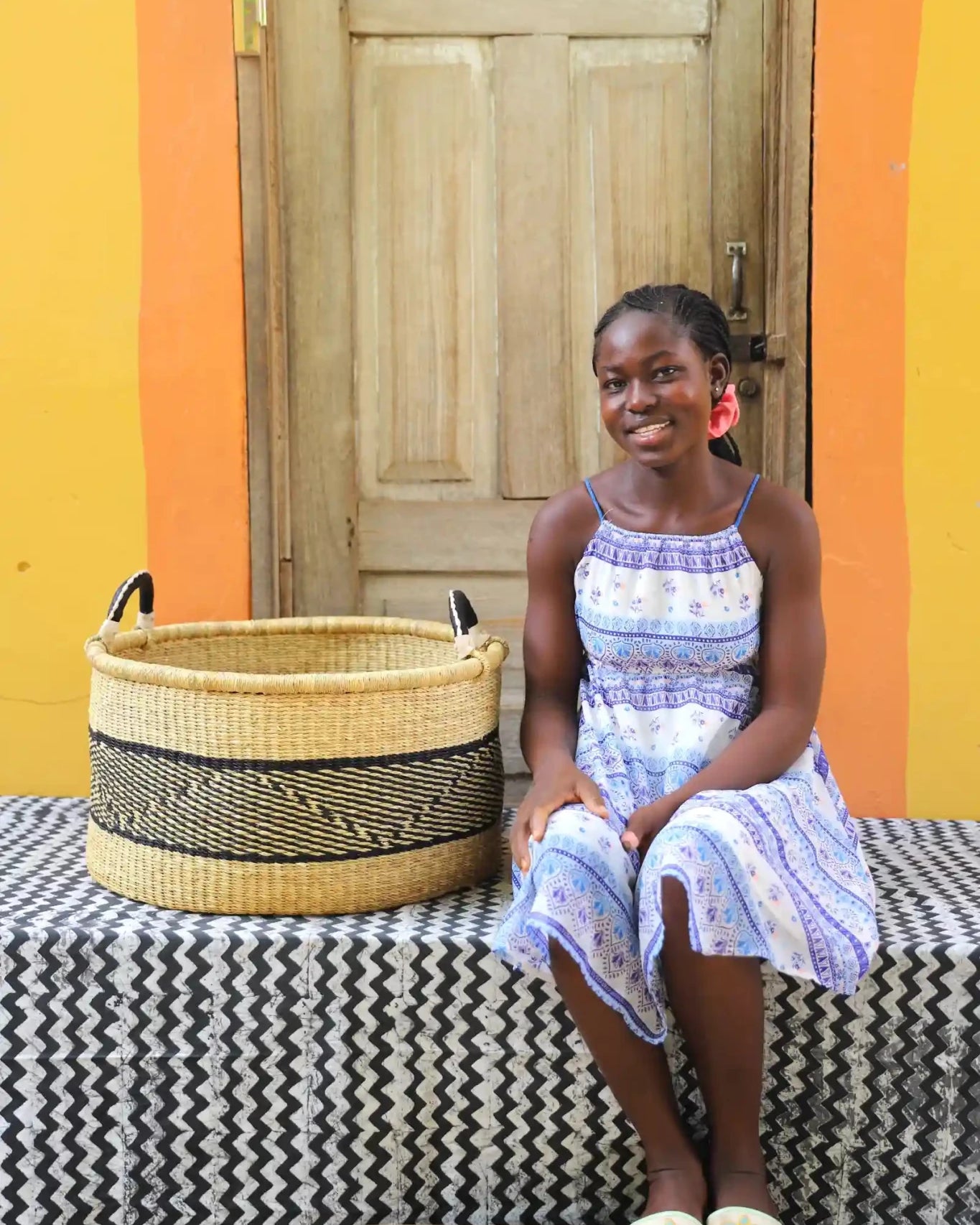 Woven Tub (Large) with woman weaver handwoven in Ghana sitting on black and white cloth and wooden door in background