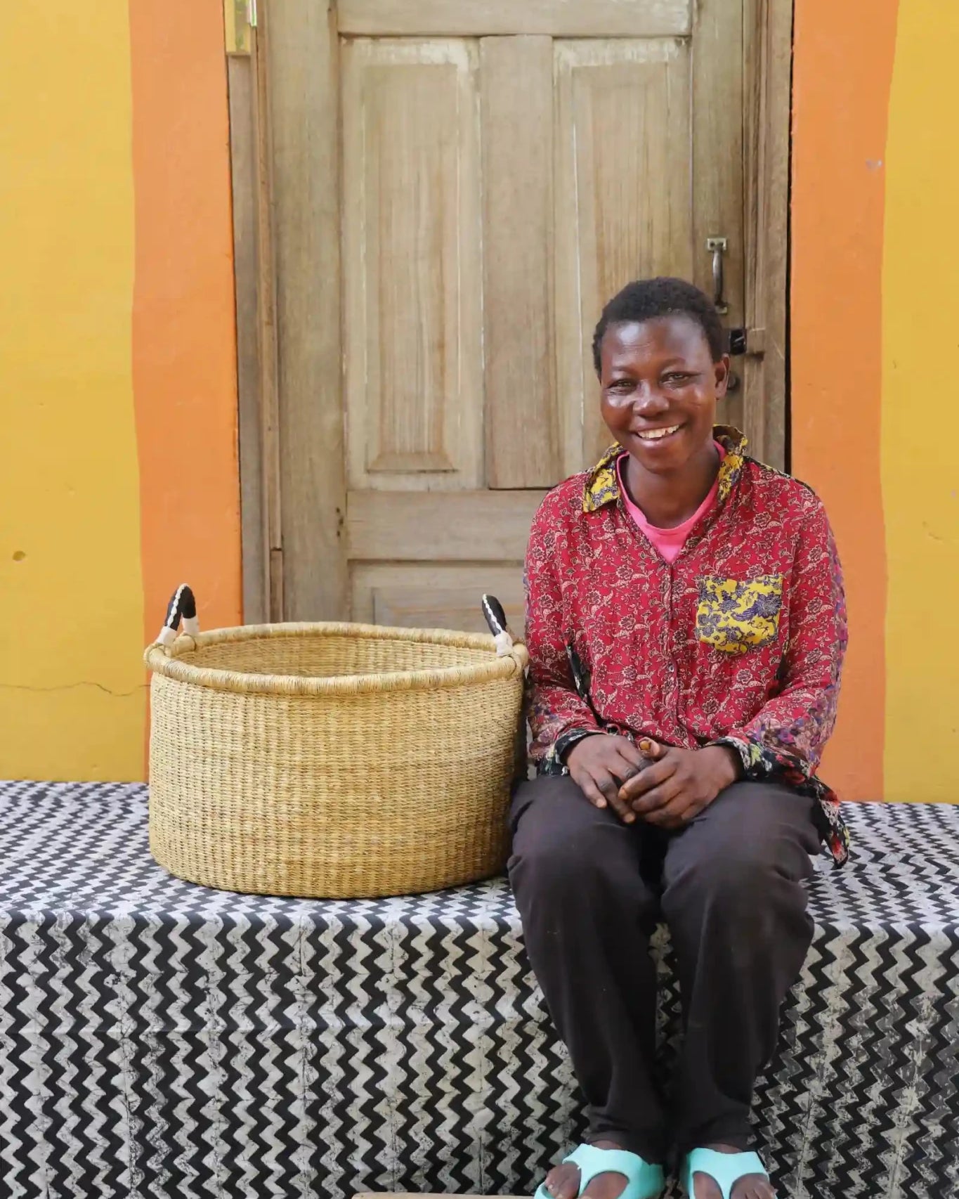 Woven Tub (Medium) with woman weaver handwoven in Ghana sitting on black and white cloth and wooden door in background