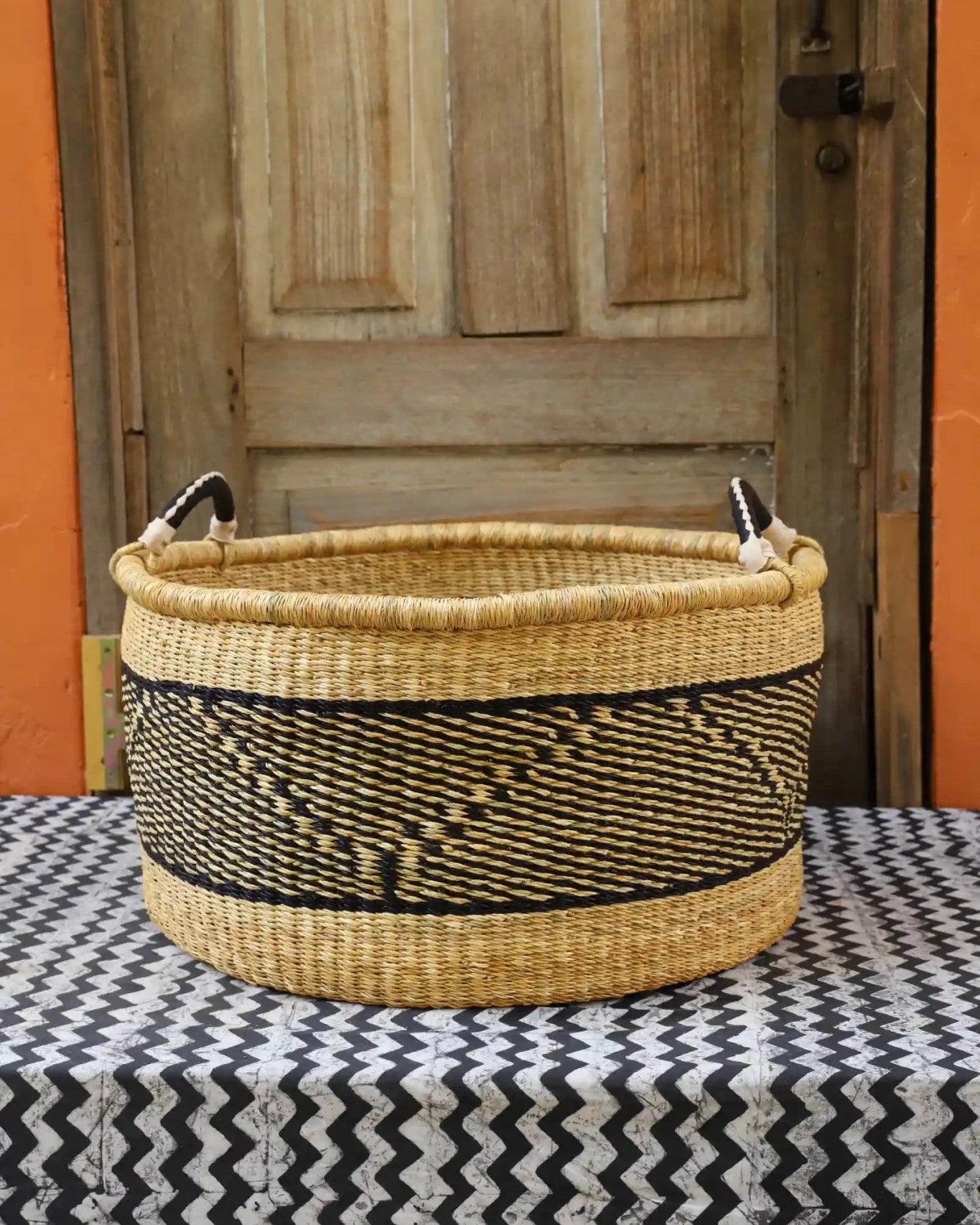 Woven Tub (Large) handwoven in Ghana sitting on black and white cloth with wooden door background