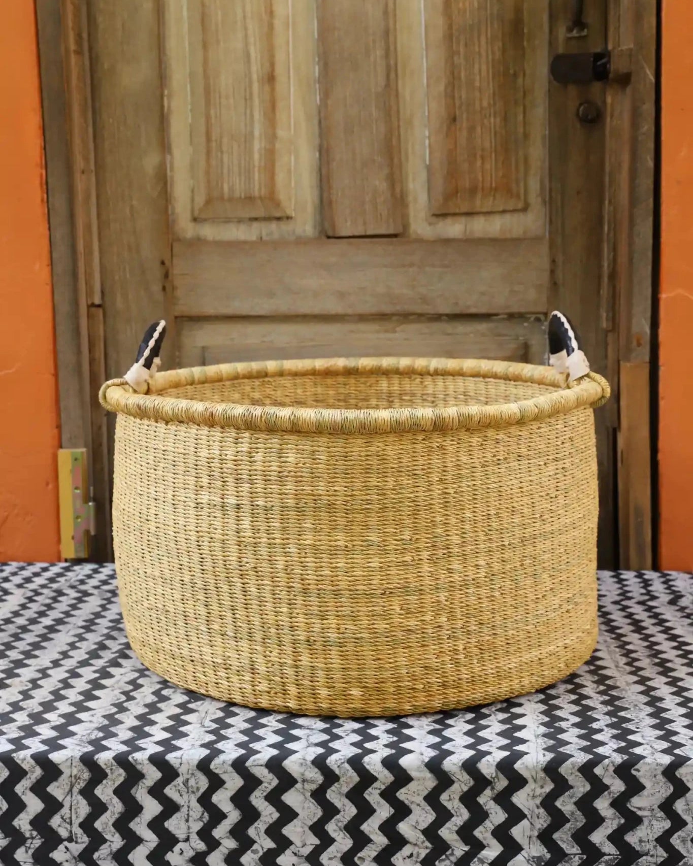Woven Tub (Large) handwoven in Ghana sitting on black and white cloth with wooden door background