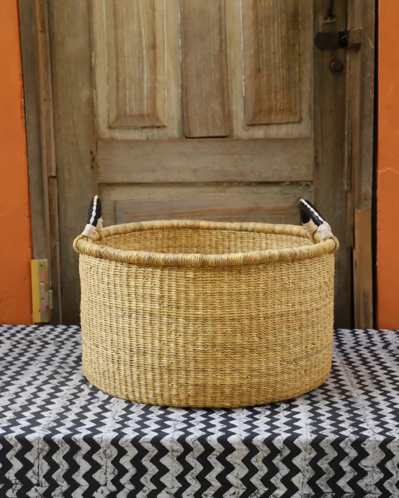 Woven Tub (Medium) handwoven in Ghana sitting on black and white cloth with wooden door background