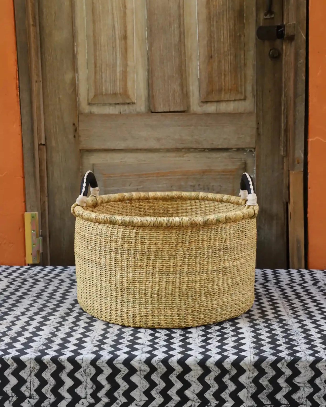 Woven Tub (Small) handwoven in Ghana sitting on black and white cloth with wooden door background