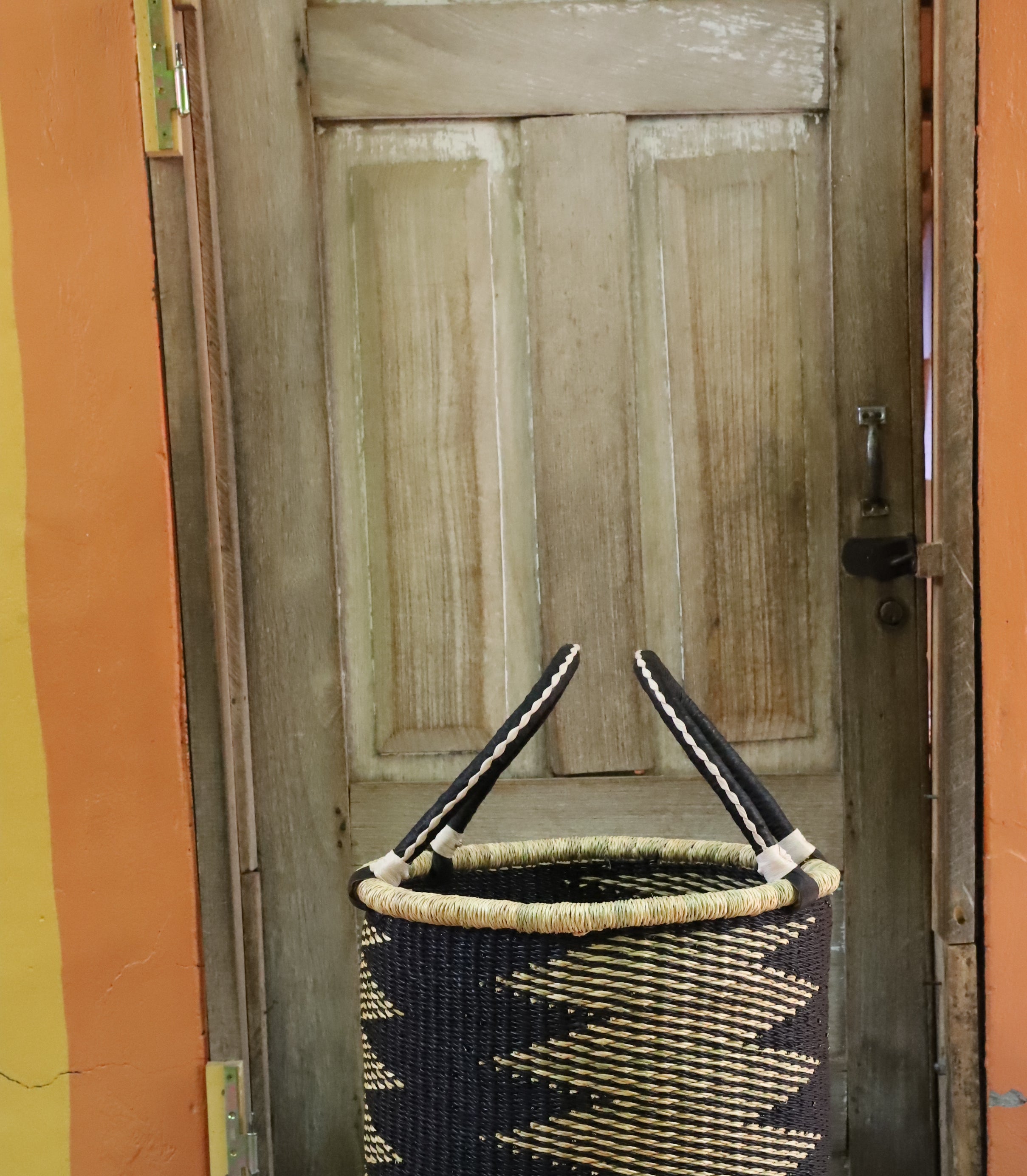 Open laundry basket in black and natural straw zigzag weave with beaded handle ends, styled on a chevron cloth.