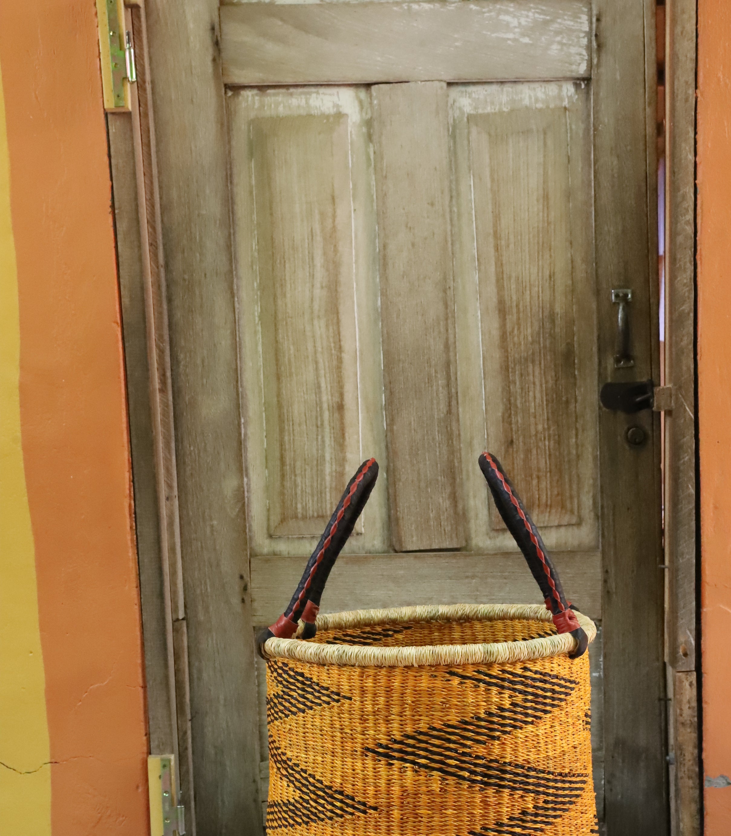 Open laundry basket in mustard and black zigzag weave with arched handles, styled on a chevron cloth.