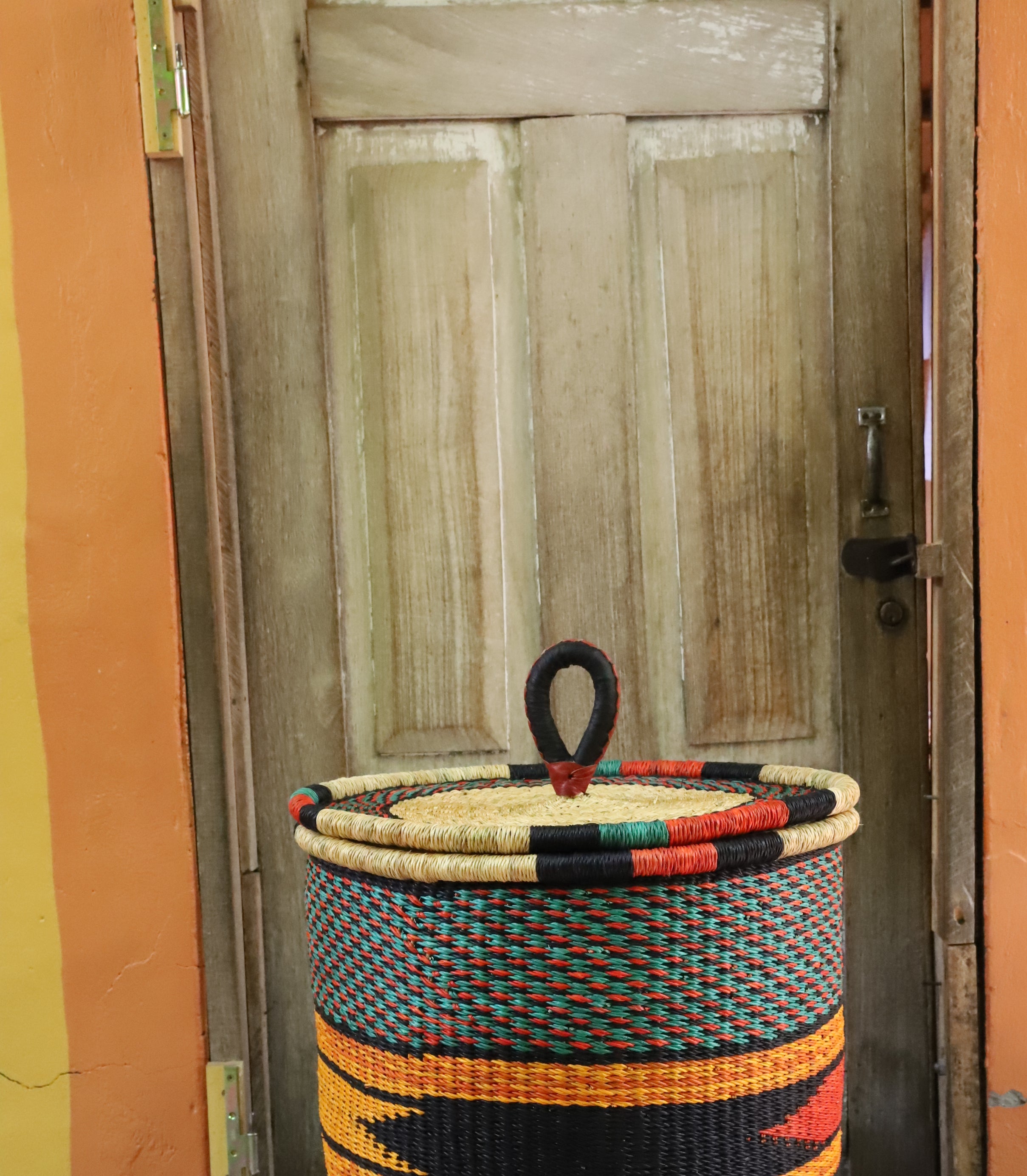 Large coiled-rim lidded laundry basket in dark weave with orange and black banding, styled on a chevron cloth.