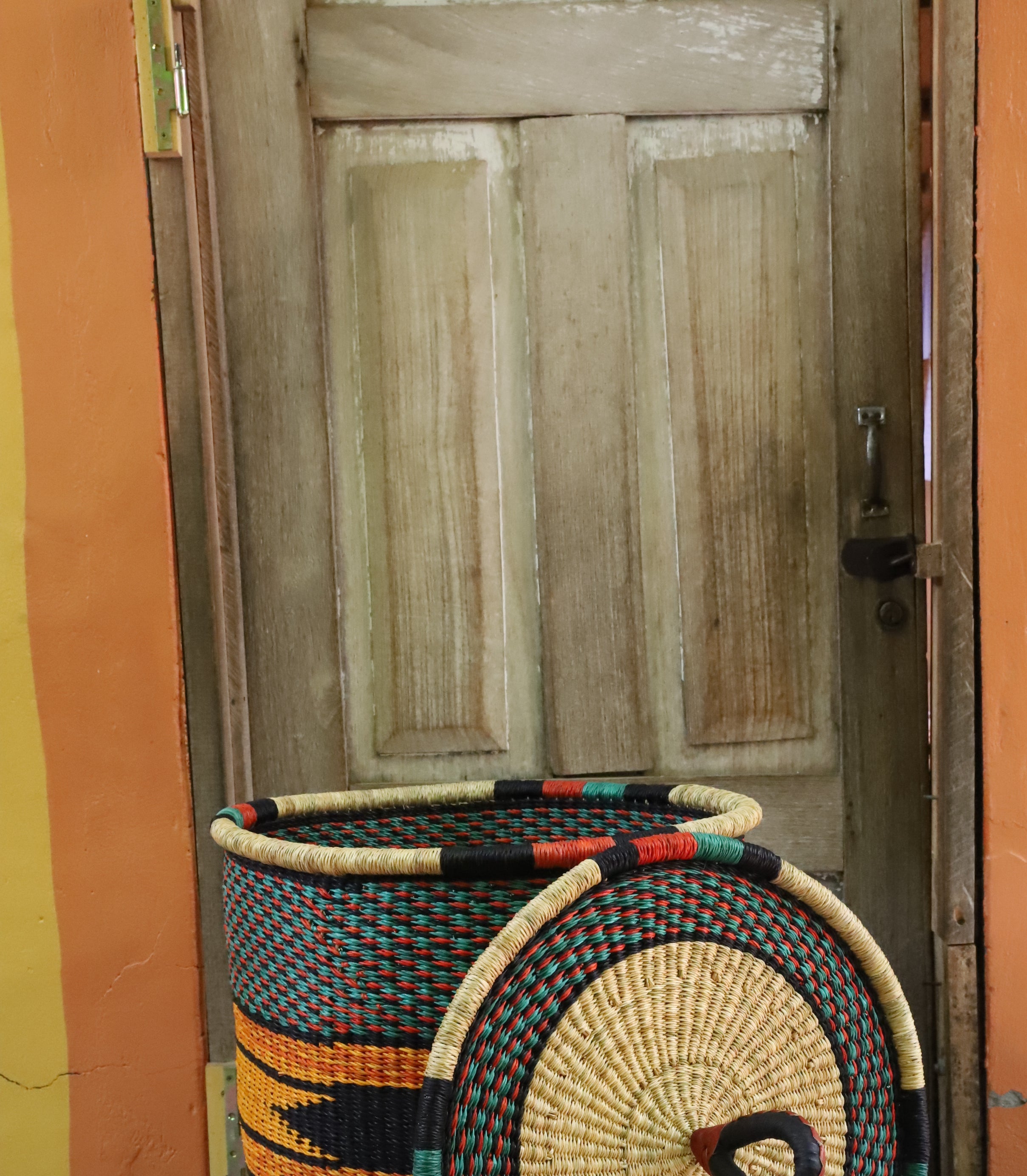Large coiled-rim laundry basket in dark weave with orange and black banding, lid resting alongside on a chevron cloth.