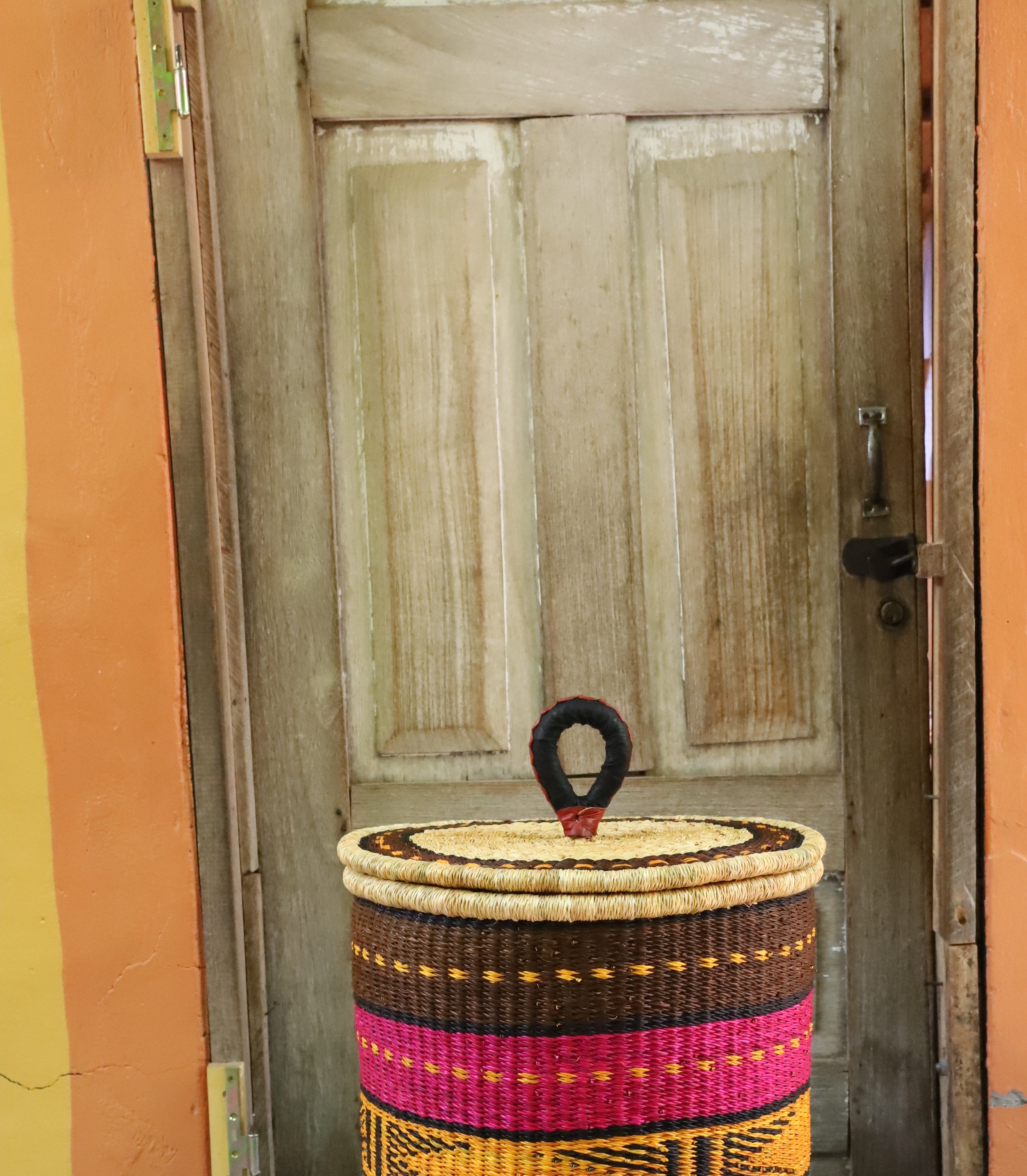 Coiled-rim lidded laundry basket in brown, pink, mustard and teal striped weave, styled on a chevron cloth.