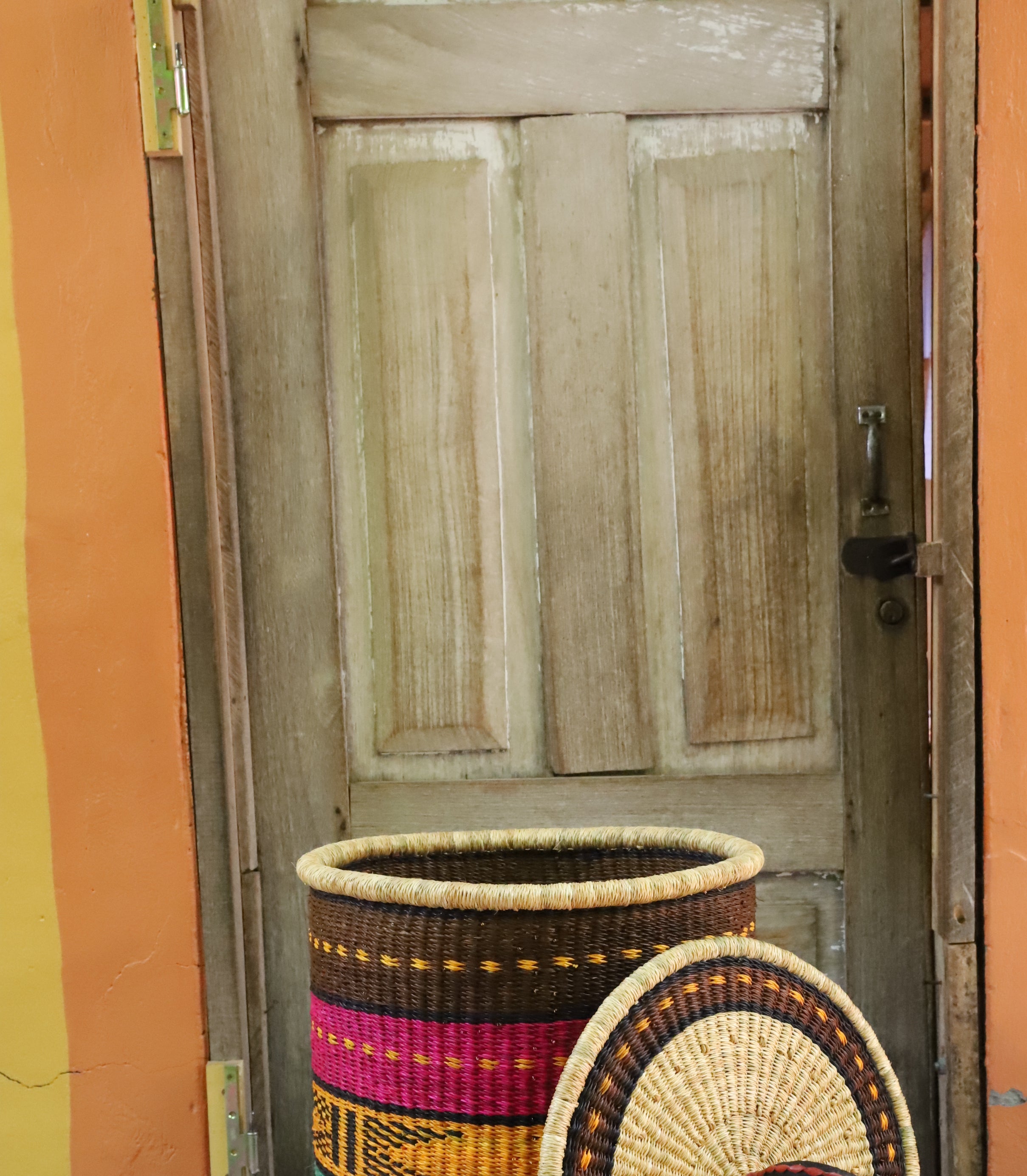 Coiled-rim laundry basket in brown, pink, mustard and teal striped weave, lid resting alongside on a chevron cloth.