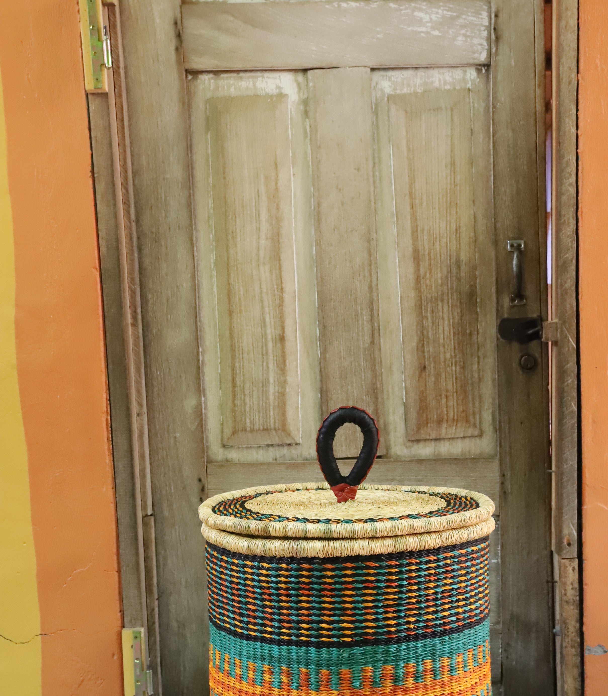 Coiled-rim lidded laundry basket in dark weave with turquoise and orange banding, styled on a chevron cloth.