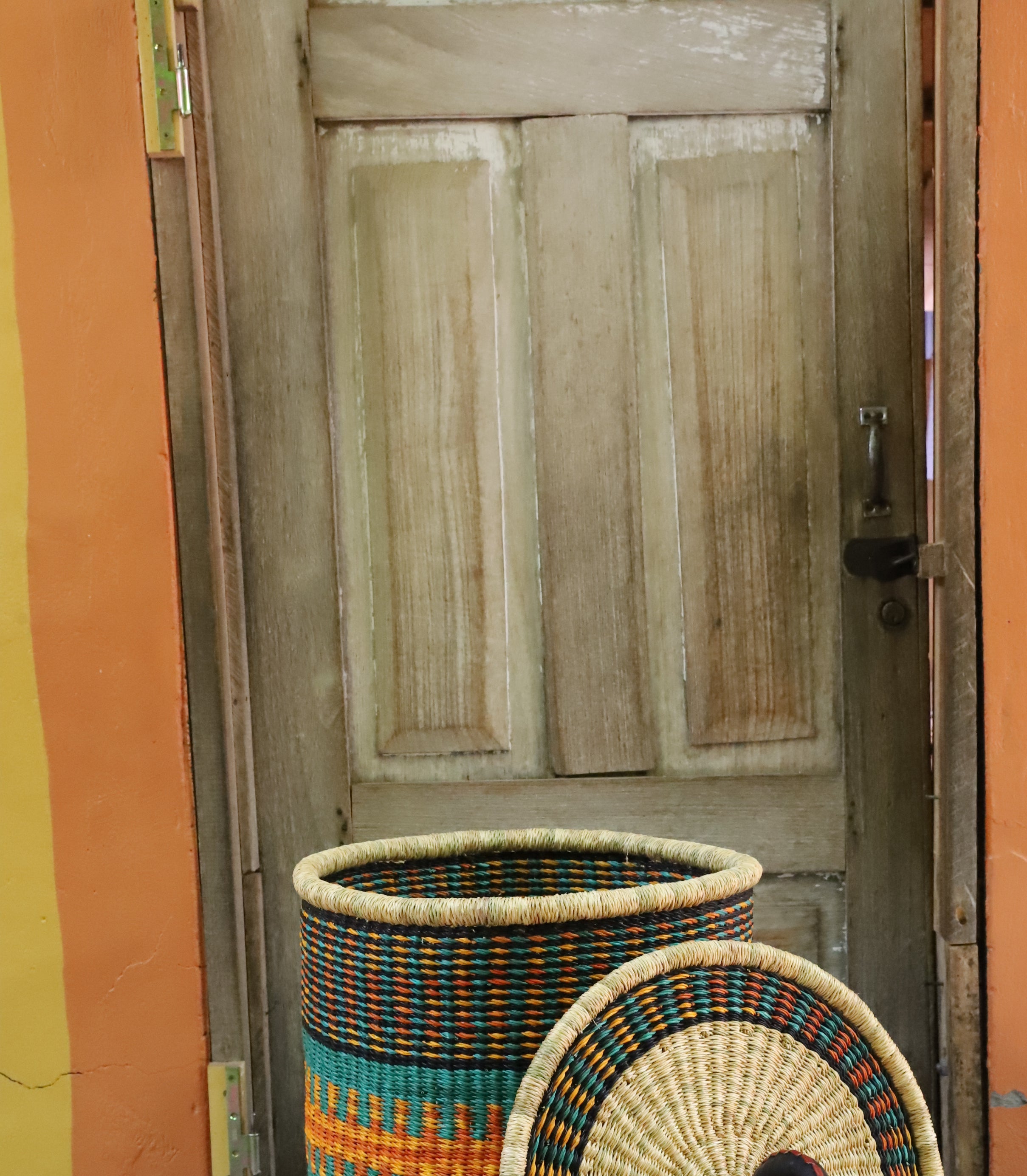 Coiled-rim laundry basket in dark weave with turquoise and orange banding, lid resting alongside on a chevron cloth.