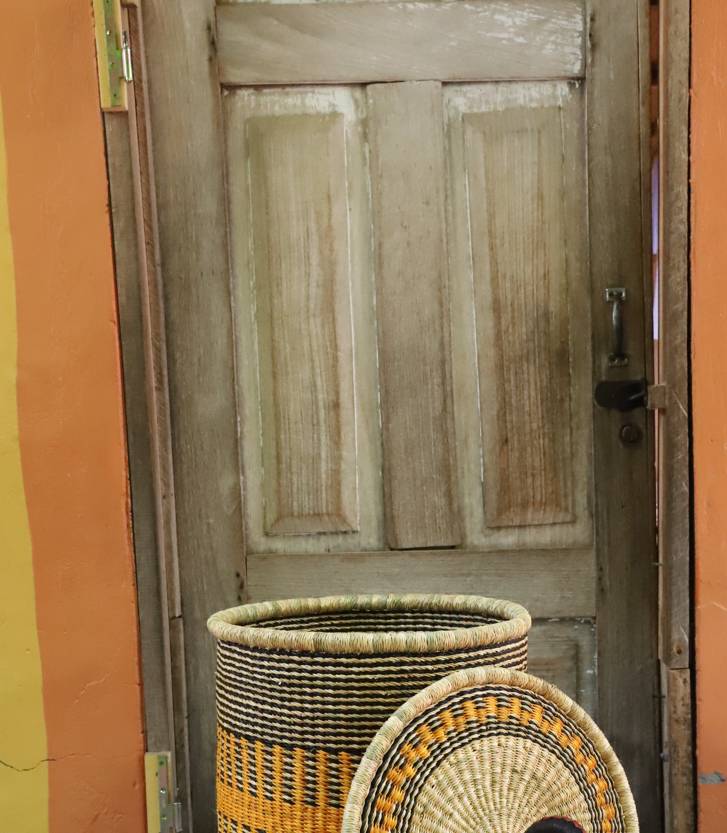 Coiled-rim laundry basket in natural straw with a striped orange band, lid resting alongside on a chevron cloth.