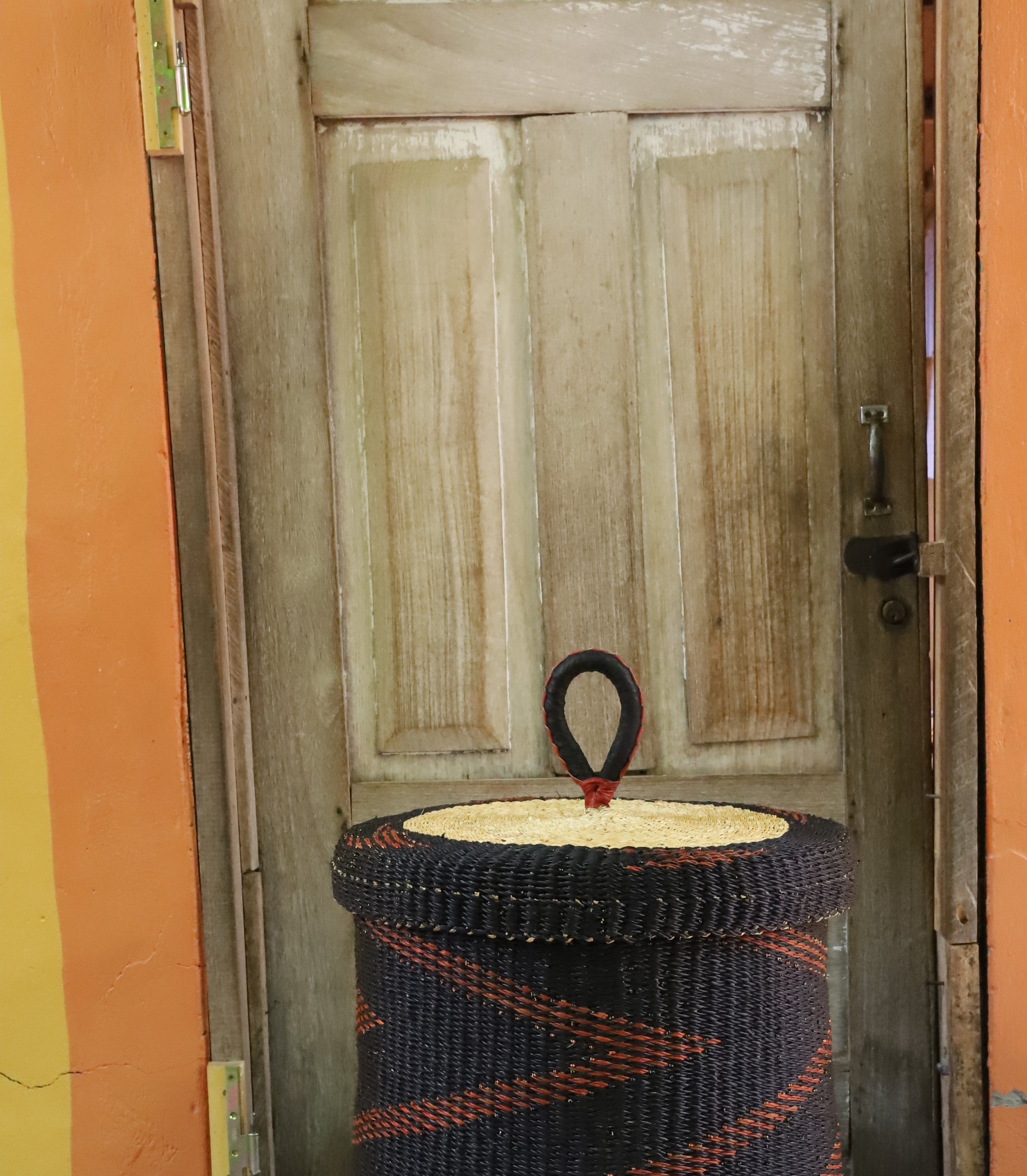 Lidded laundry basket in dark brown elephant grass with a rust zigzag weave, styled on a chevron cloth.