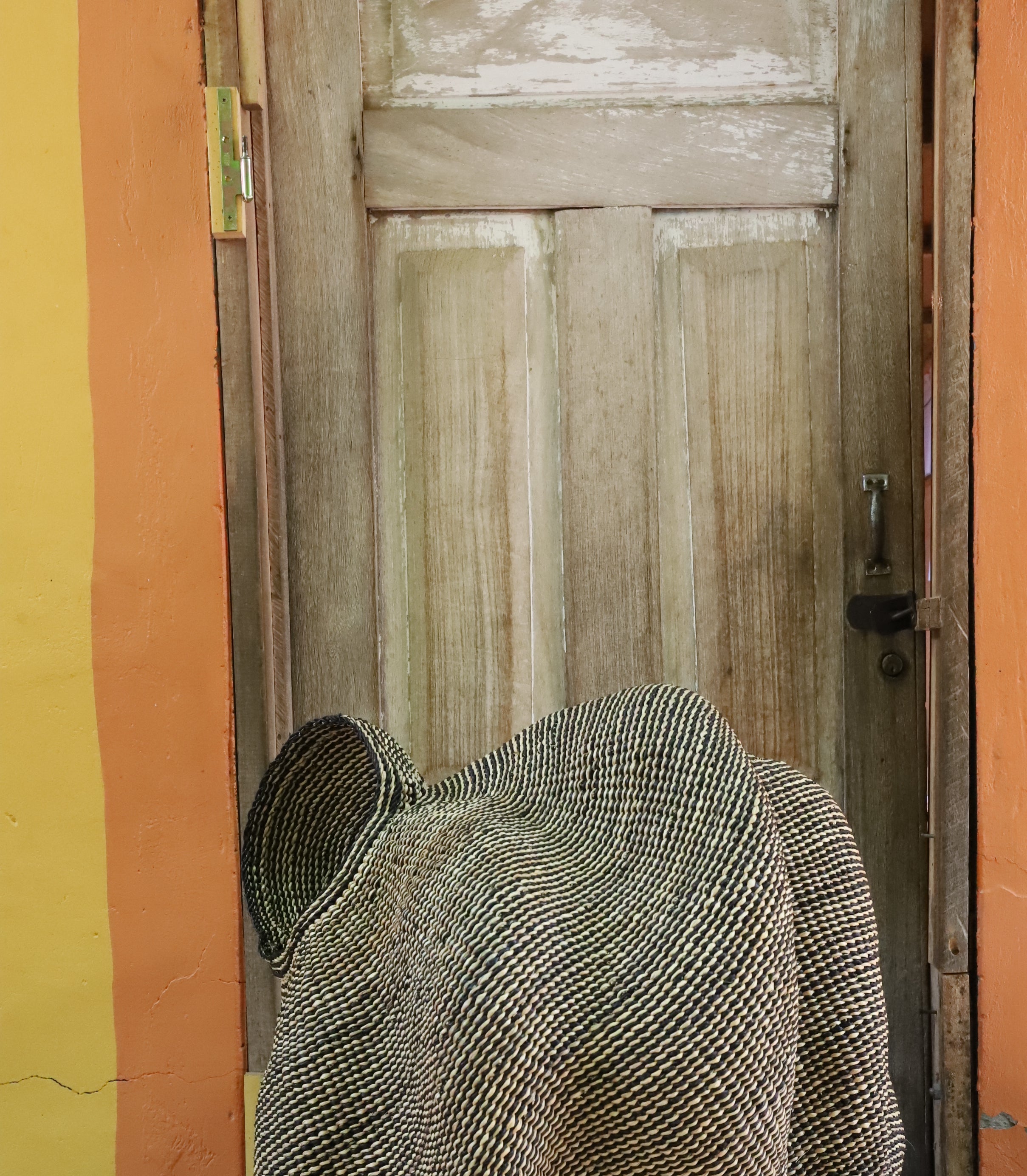 Large sculptural Bolga basket in a dense woven spiral form, natural straw, shown from behind on a chevron cloth.