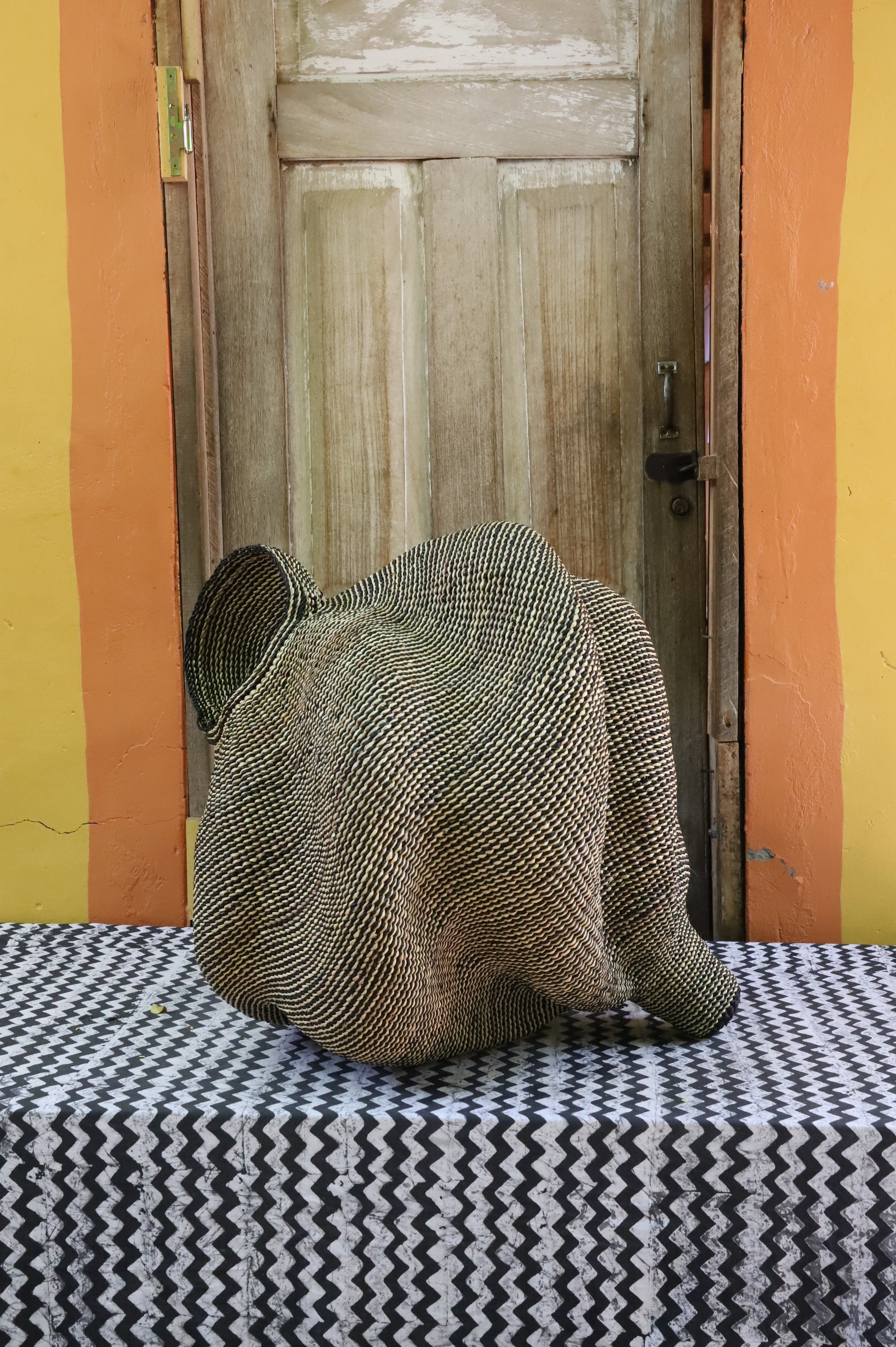 Large sculptural Bolga basket in a dense woven spiral form, natural straw, shown from behind on a chevron cloth.