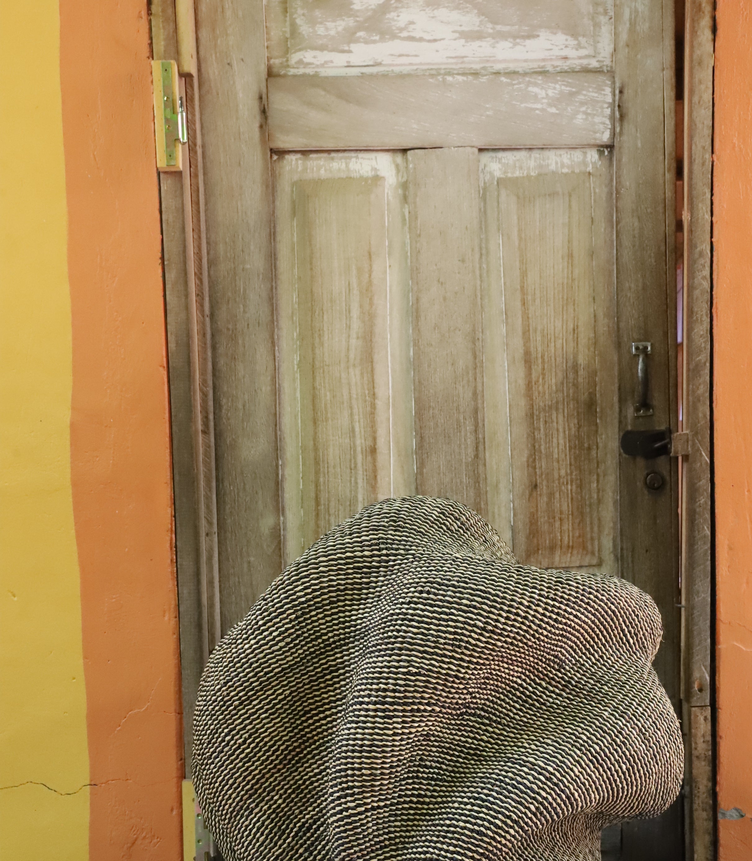 Densely coiled spiral Bolga basket in natural straw, textured woven surface, styled by a wooden door.