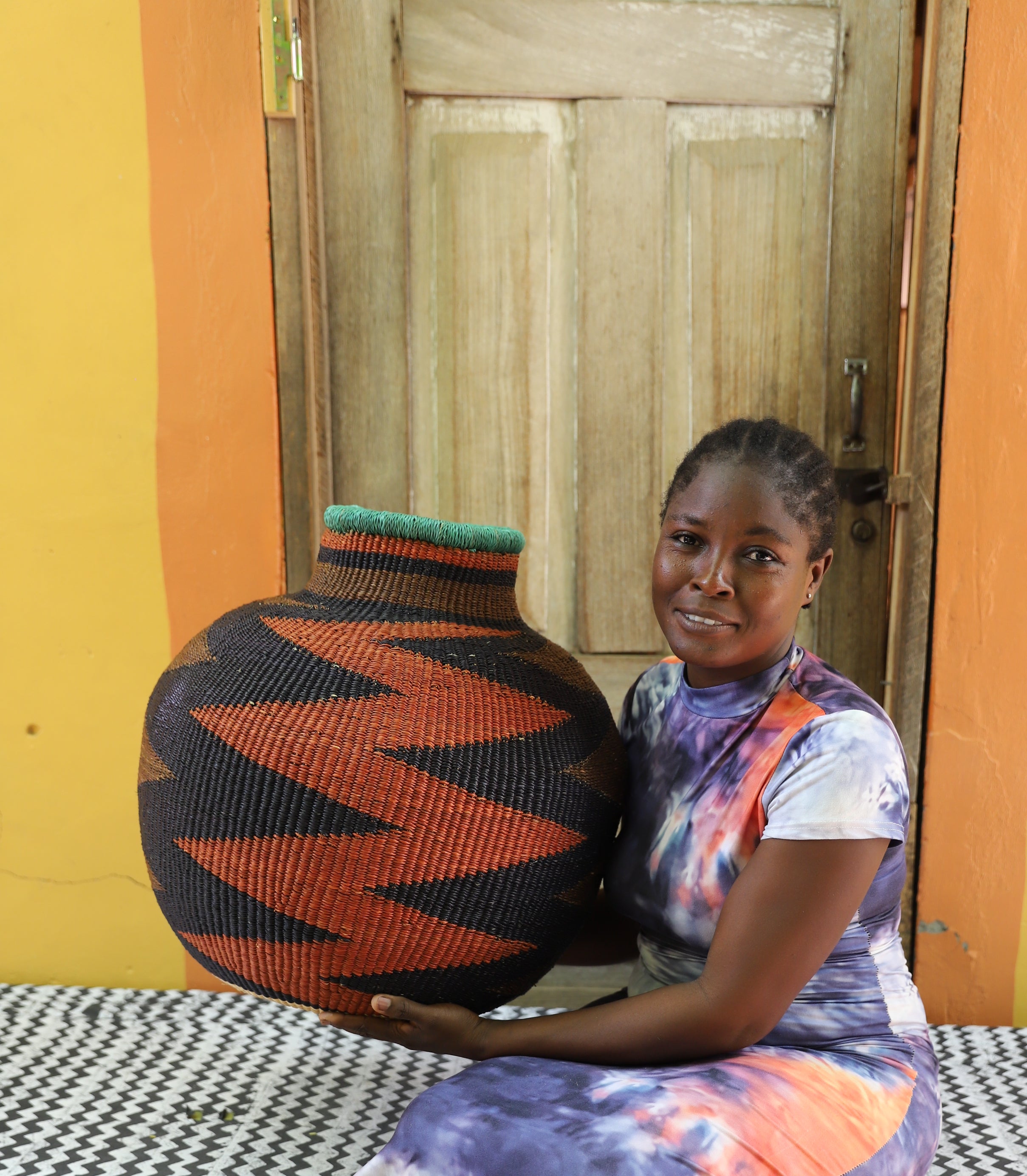 Bulbous 10 Cows décor basket in black and rust zigzag weave, held by a seated person for scale.