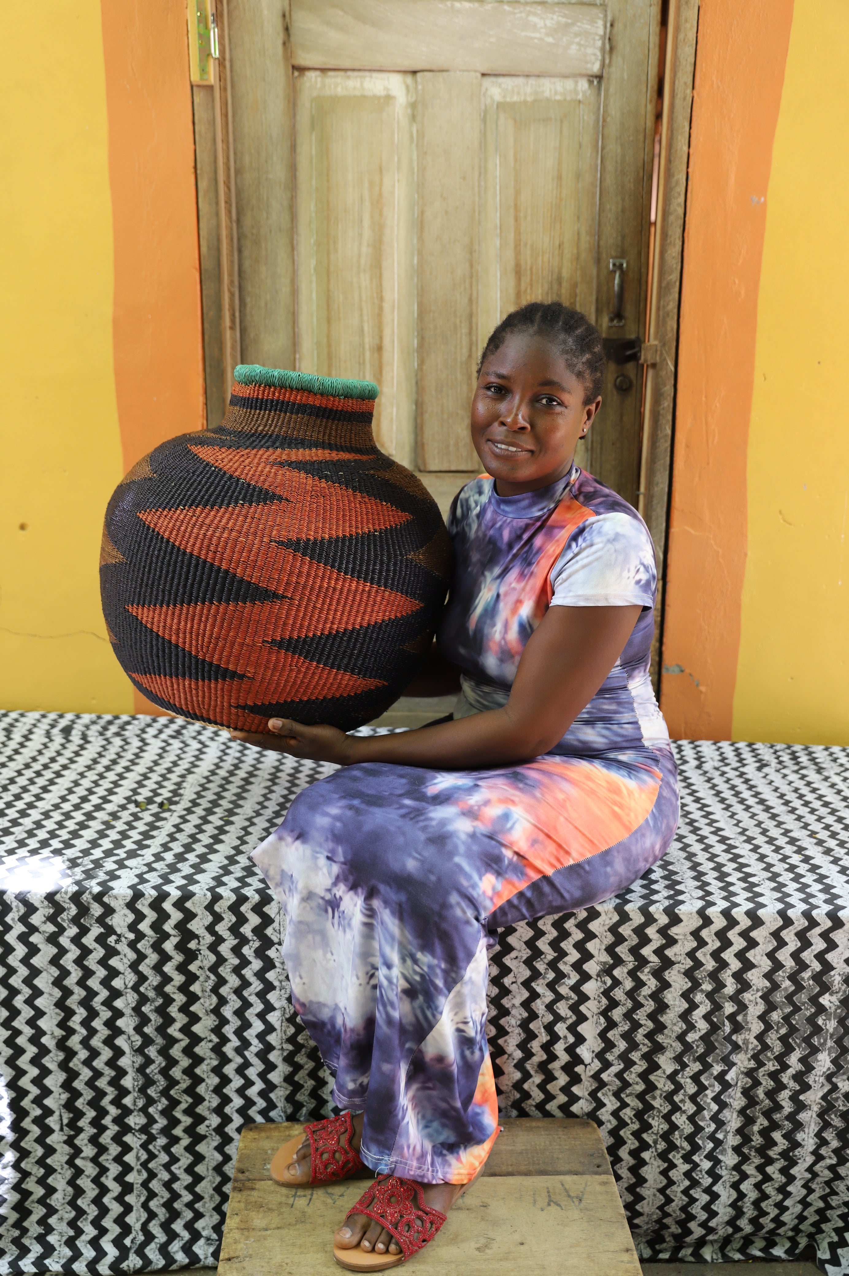 Bulbous 10 Cows décor basket in black and rust zigzag weave, held by a seated person for scale.
