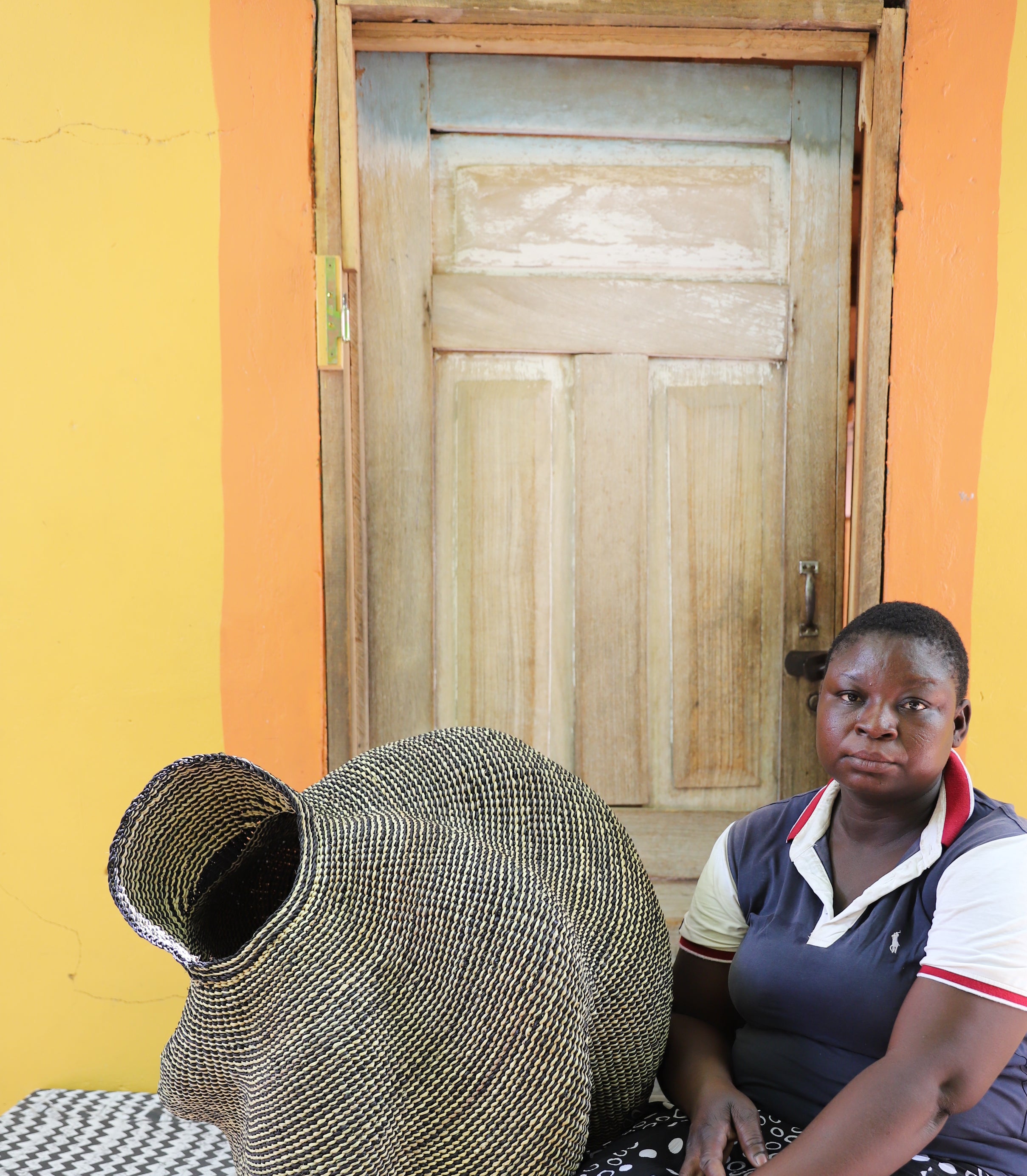 Large spiral-form Bolga basket in natural straw, shown beside a seated person for scale.