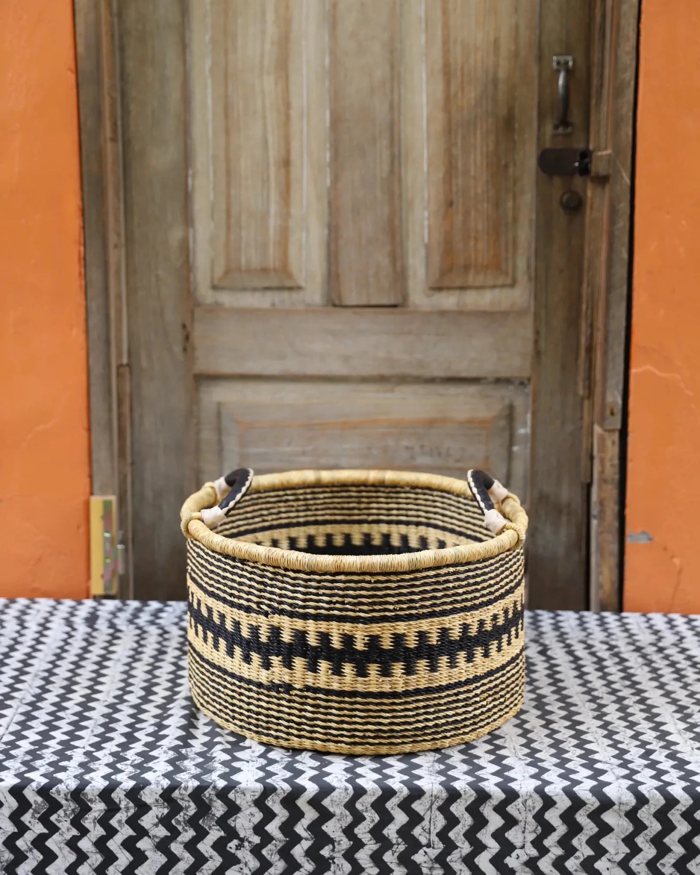 Woven Tub (Small) handwoven in Ghana sitting on black and white cloth with wooden door background
