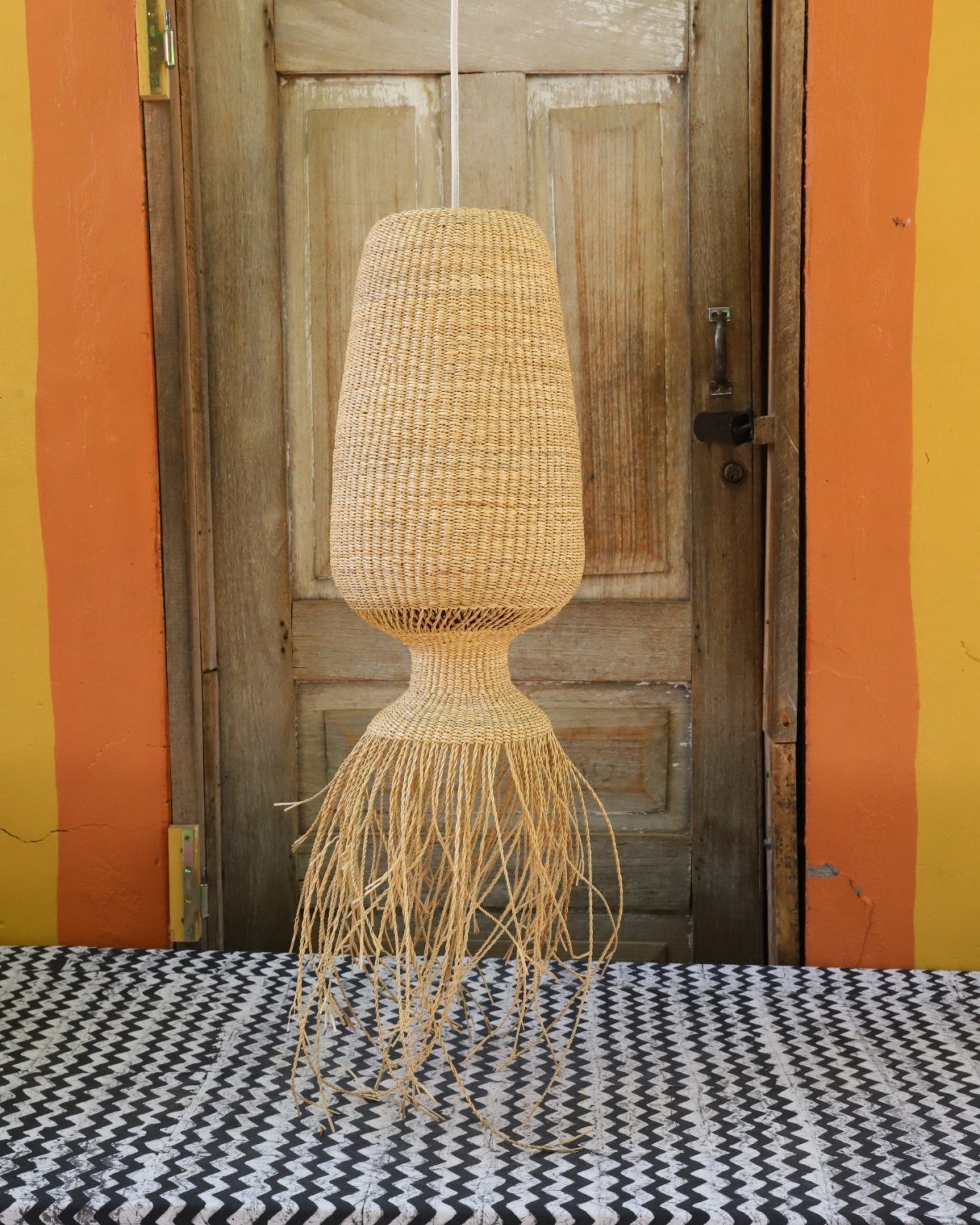 Woven lamp against a wooden wall with colorful striped background