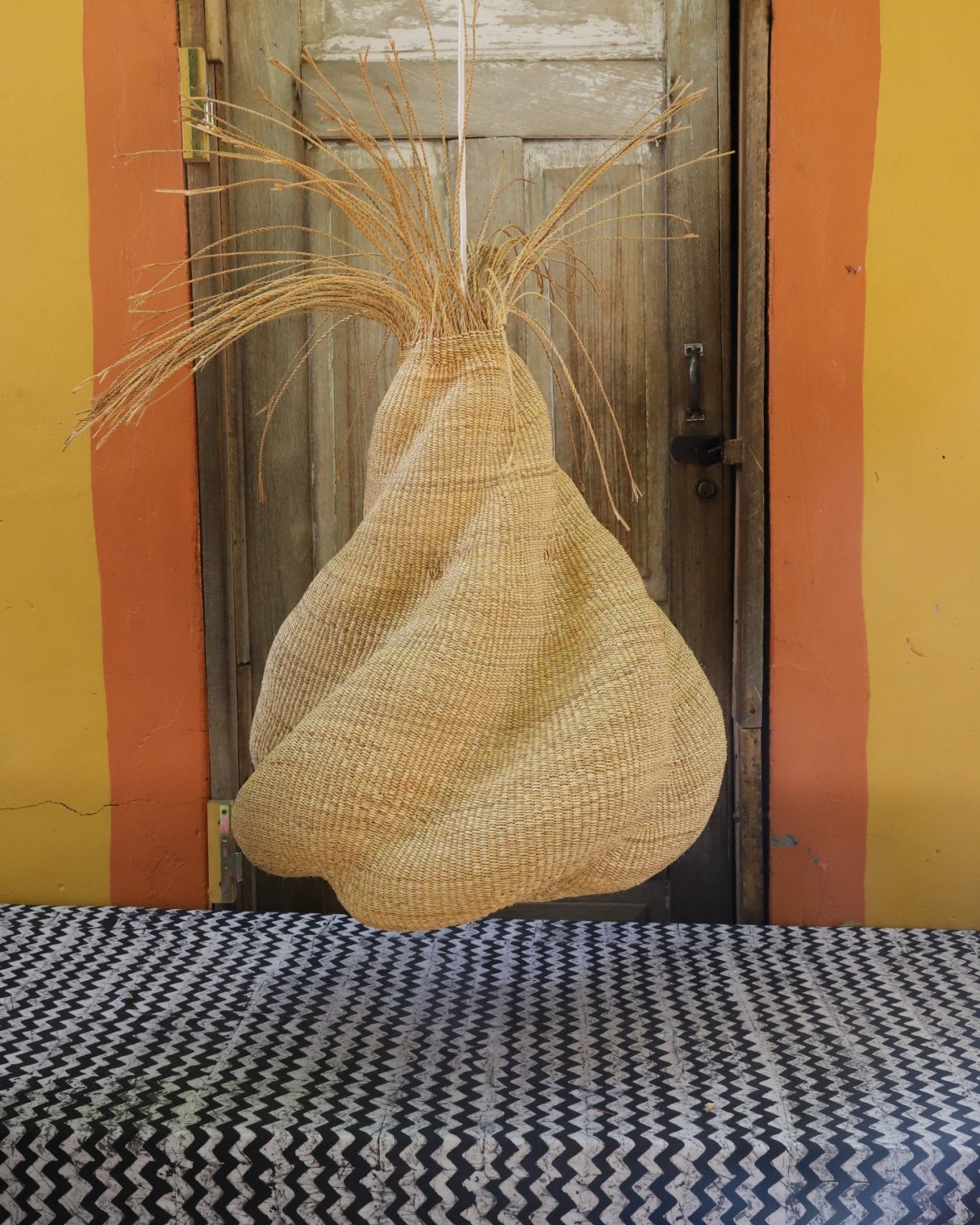 Woven lamp hanging on a wooden shelf with a colorful wall background
