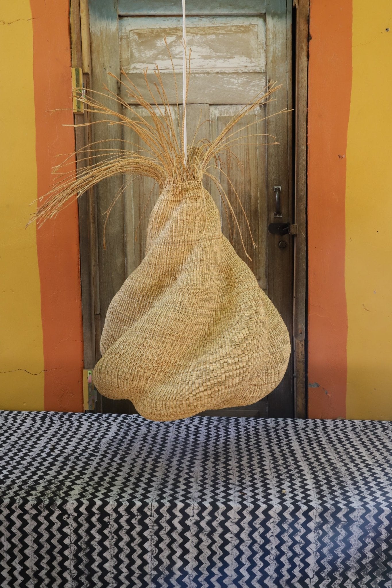 Woven lamp hanging on a wooden shelf with a colorful wall background