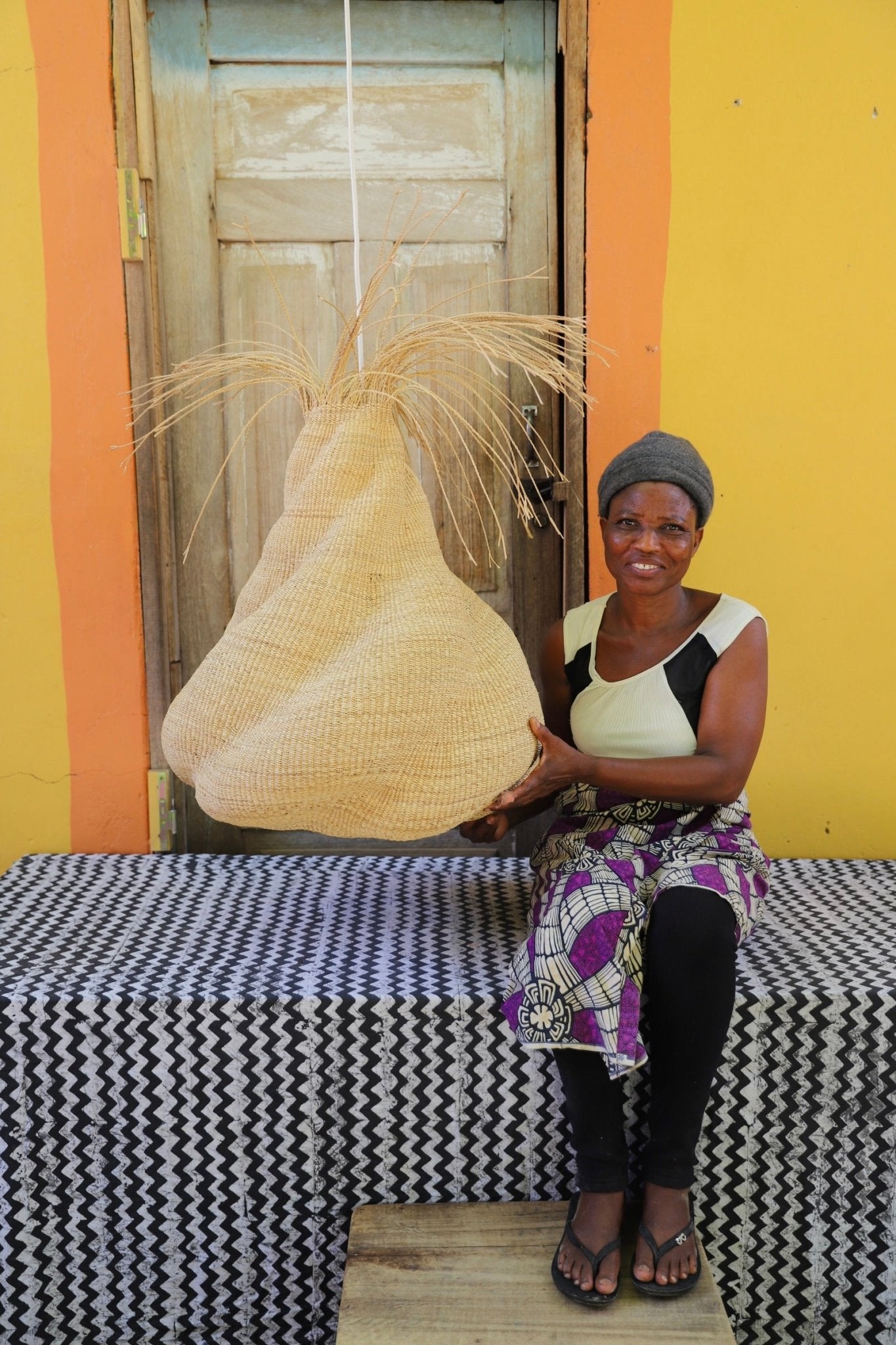 Woman sitting on a bench with a woven basket in front of a yellow wall.