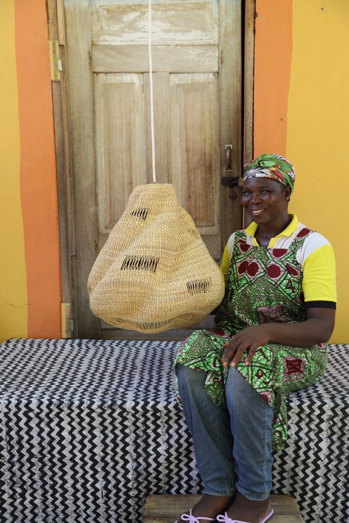 Woman sitting on a bench holding a woven basket against a colorful wall.