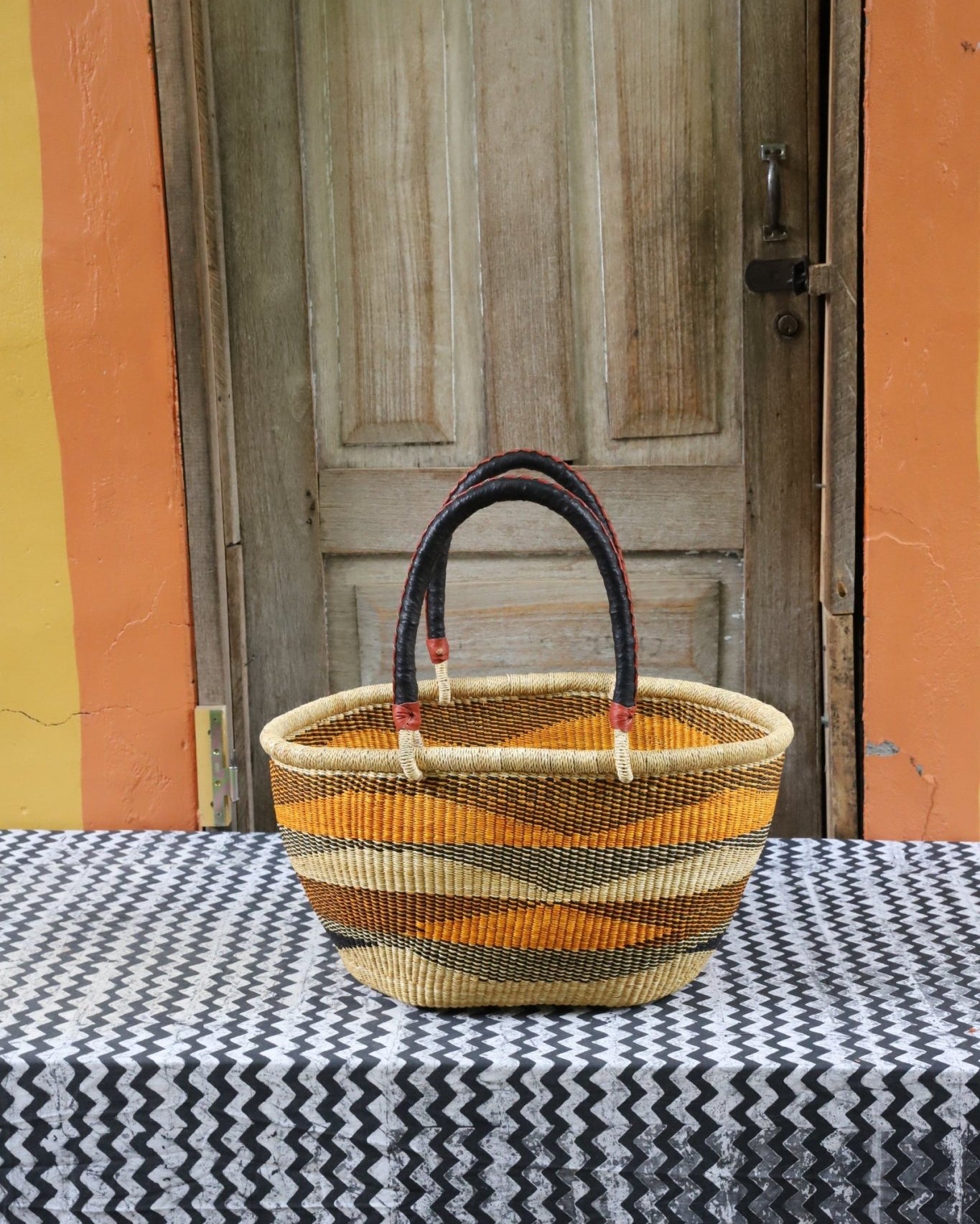 Woven carry on bag with premium leather handles on a black and white cloth against a wooden door.