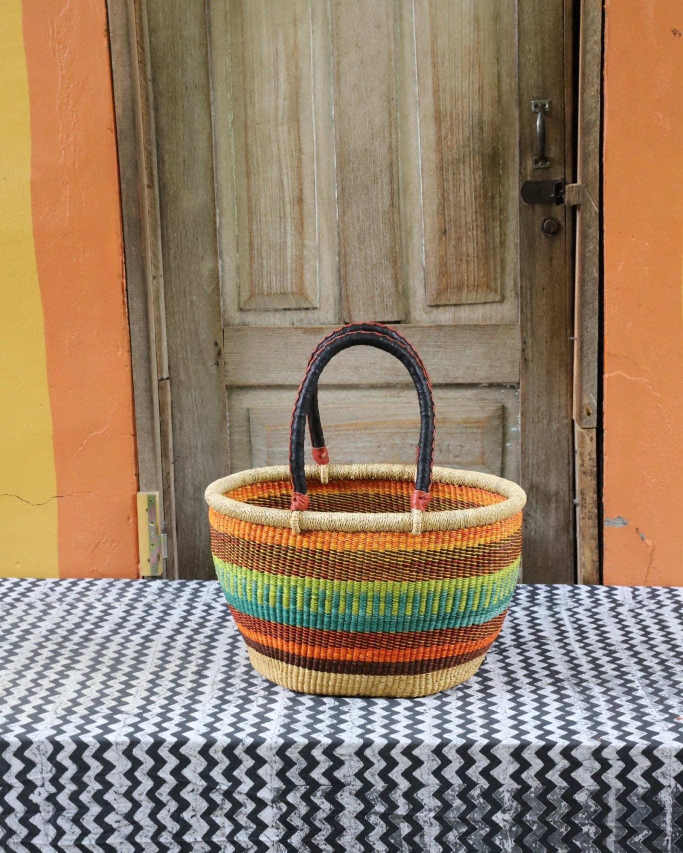 Woven carry on bag with premium leather handles on a black and white cloth against a wooden door.