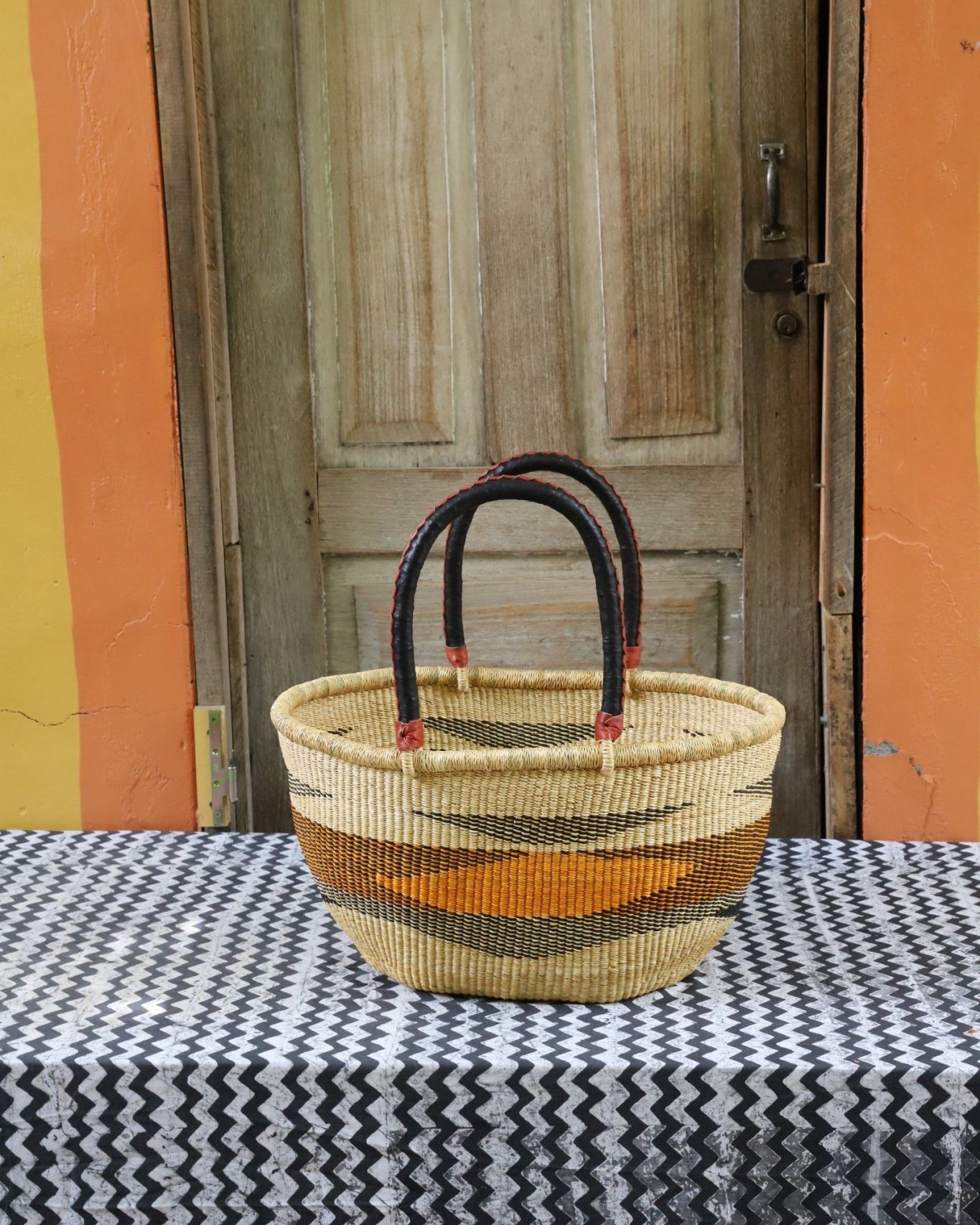 Woven carry on bag with premium leather handles on a black and white cloth against a wooden door.