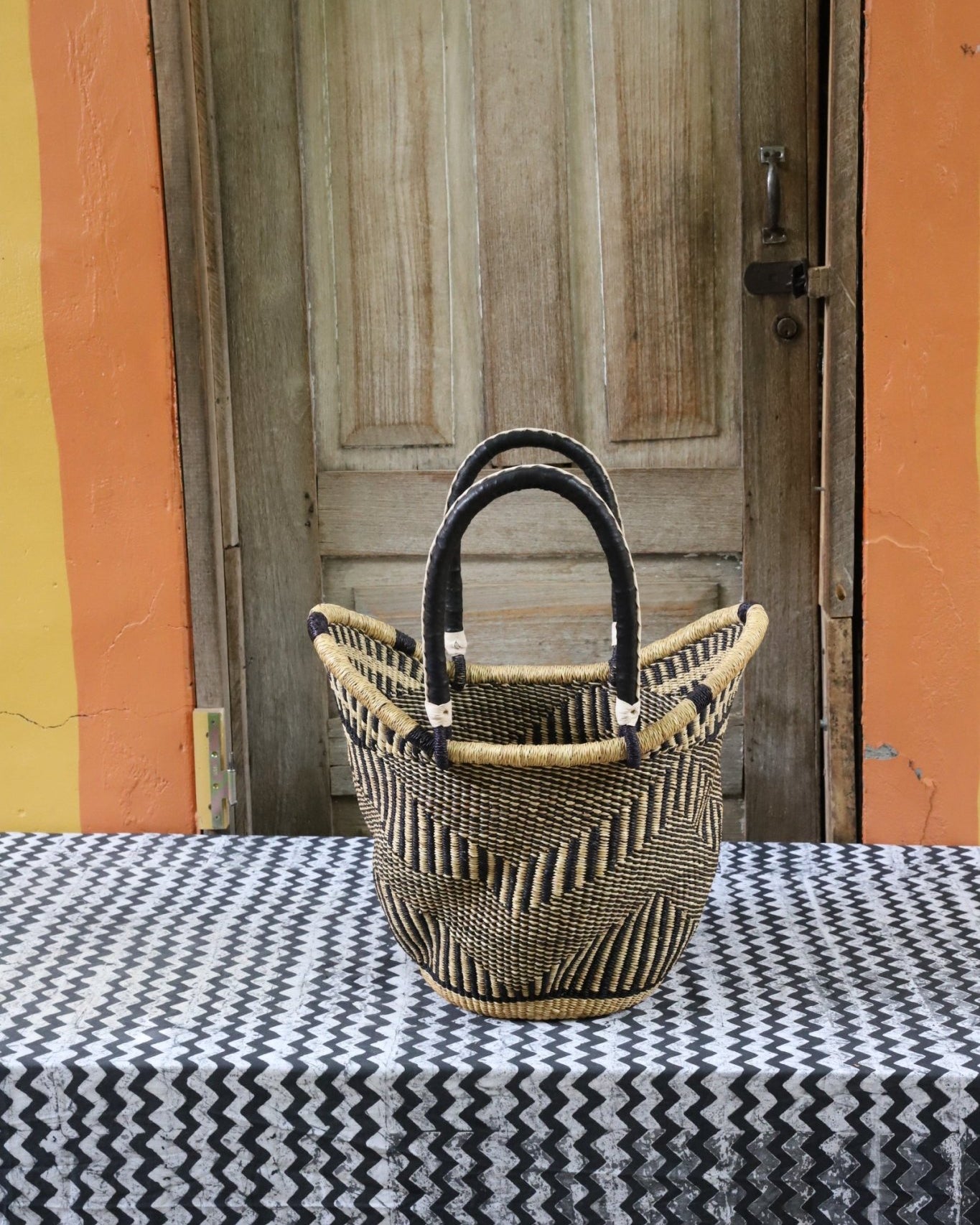 Woven carry on basket with premium leather on a black and white cloth against a wooden door