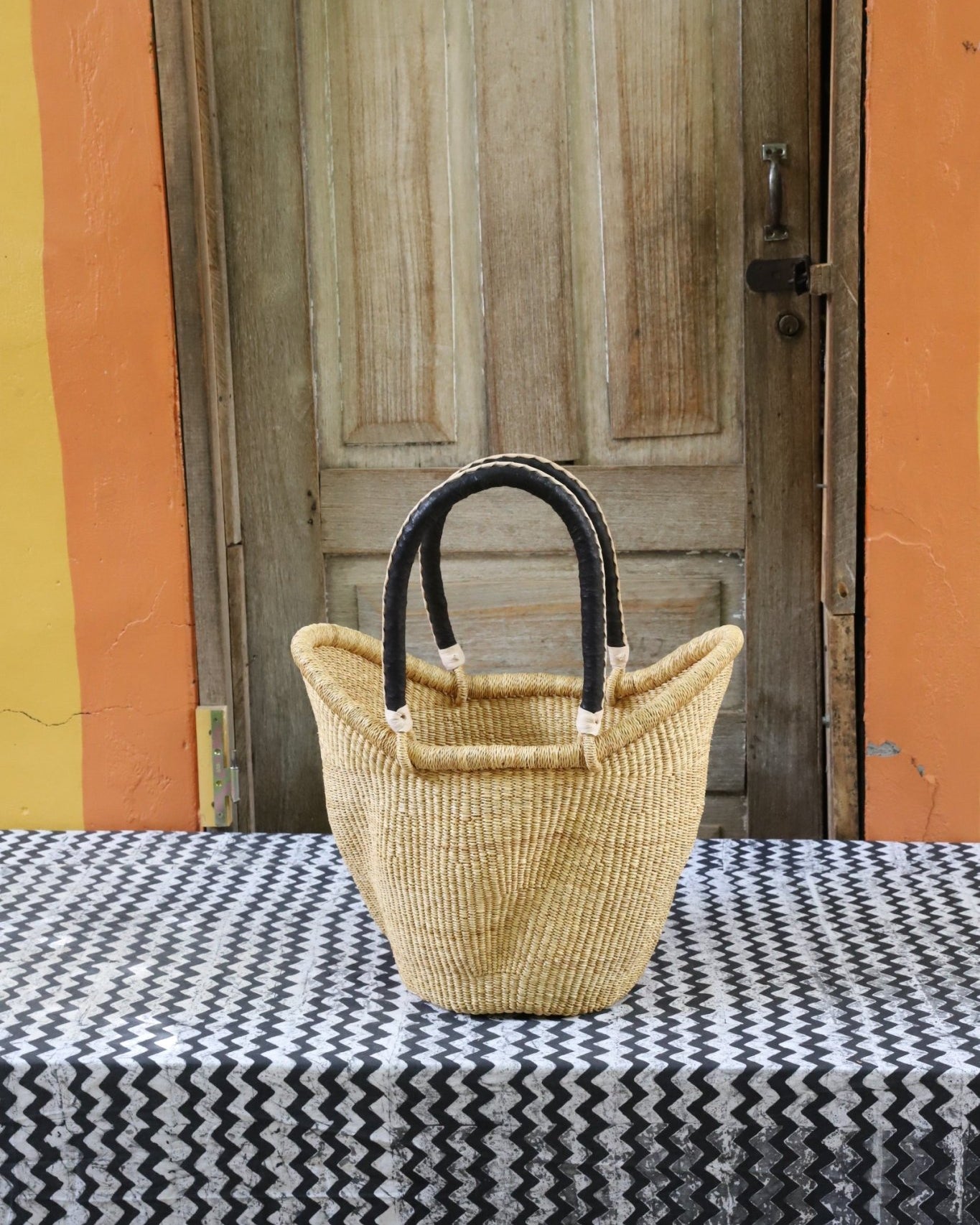 Woven carry on basket with premium leather on a black and white cloth against a wooden door