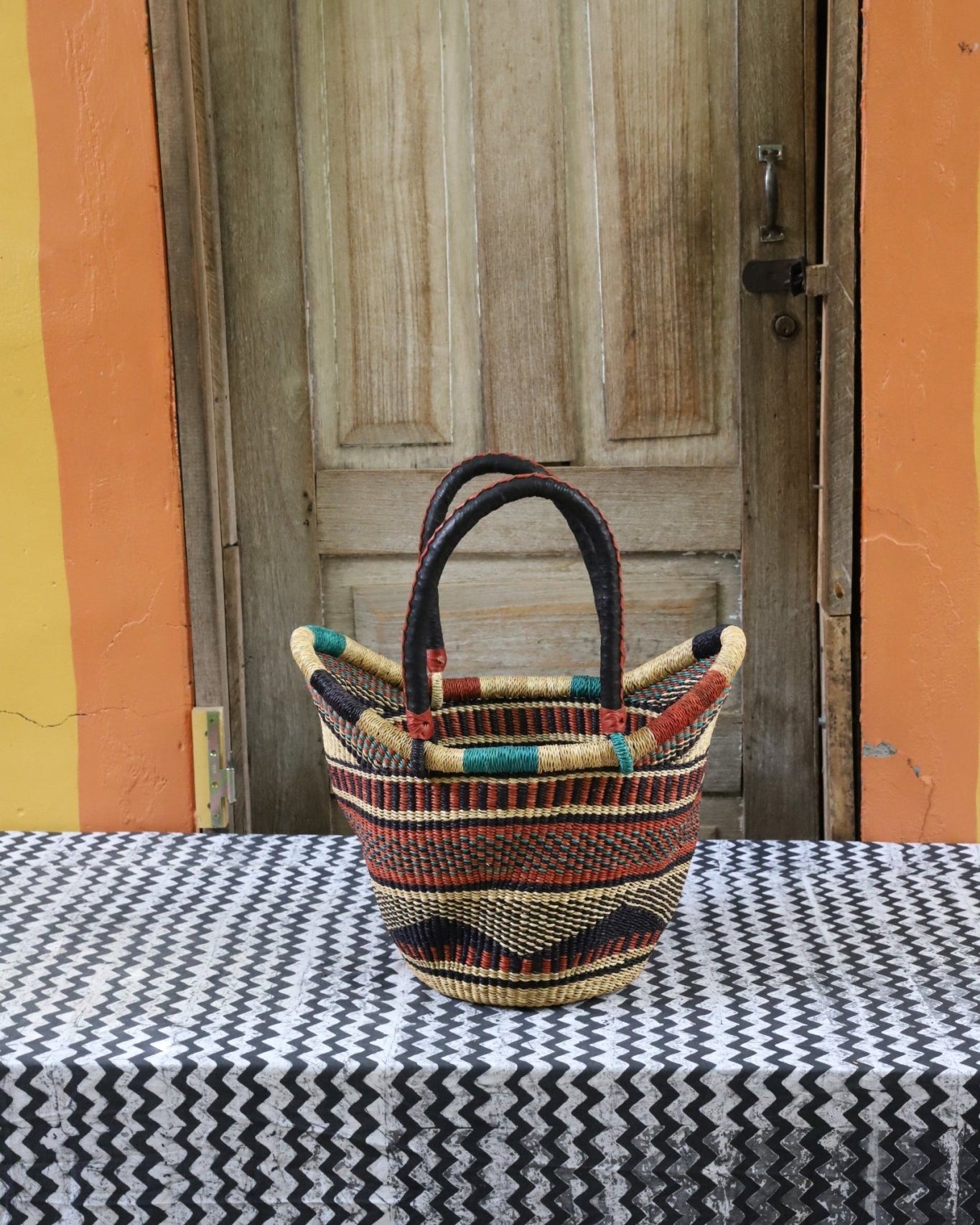 Woven carry on basket with premium leather on a black and white cloth against a wooden door