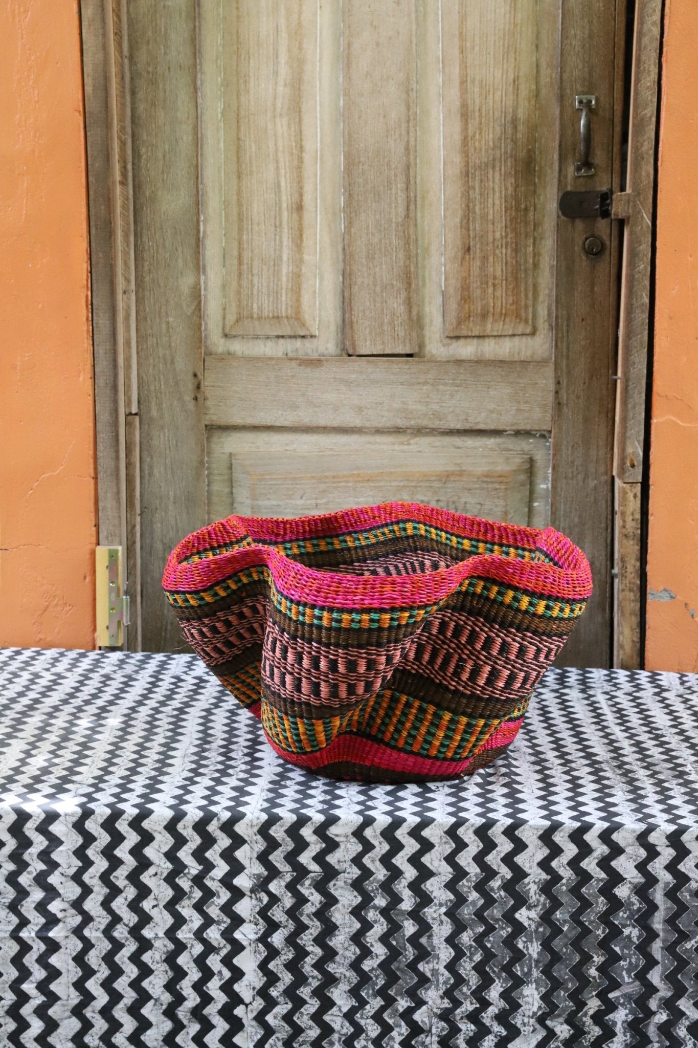 Decorative handwoven straw basket with colorful patterns on a black and white cloth against a wooden door.