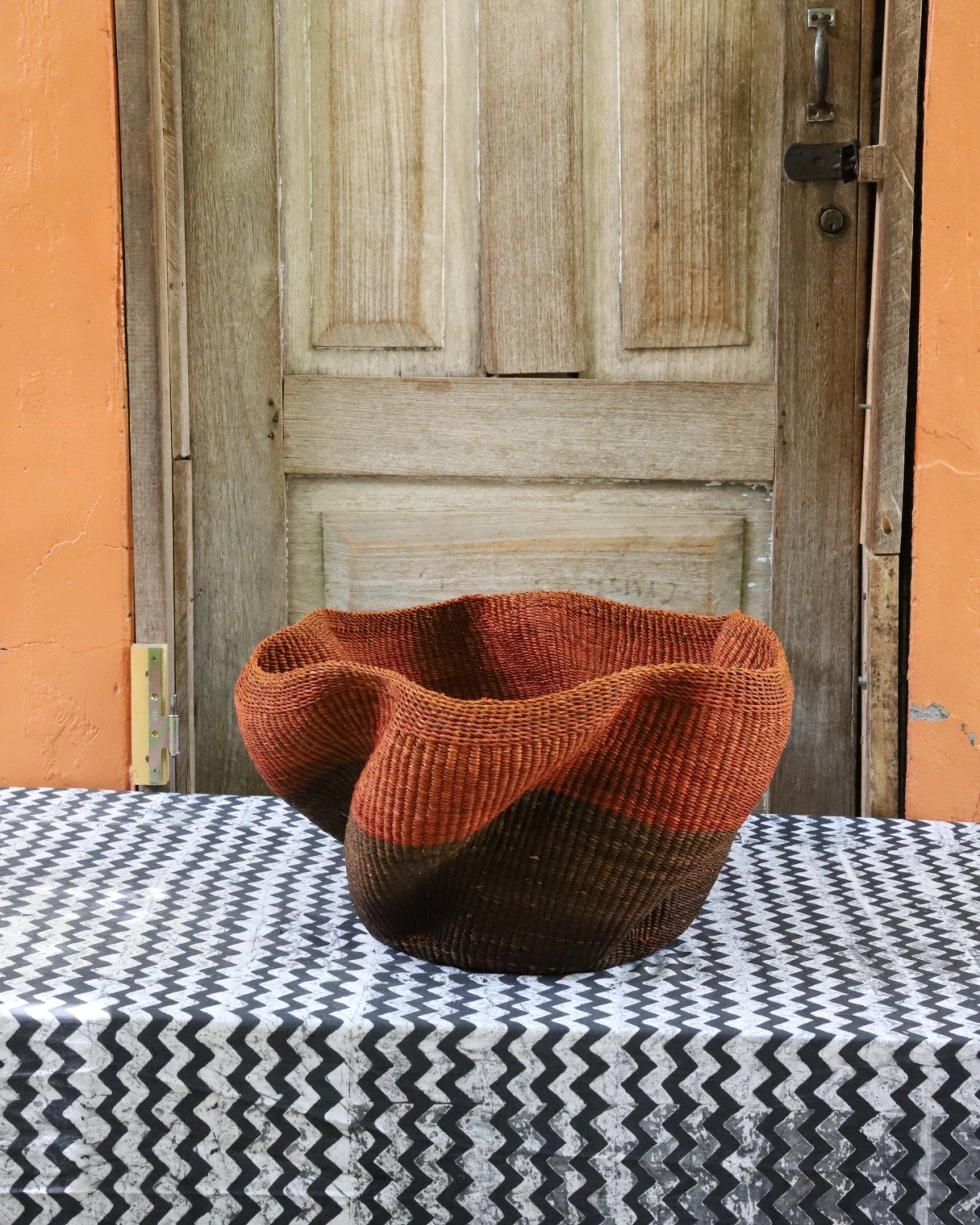 Decorative handwoven straw basket with colorful patterns on a black and white cloth against a wooden door.
