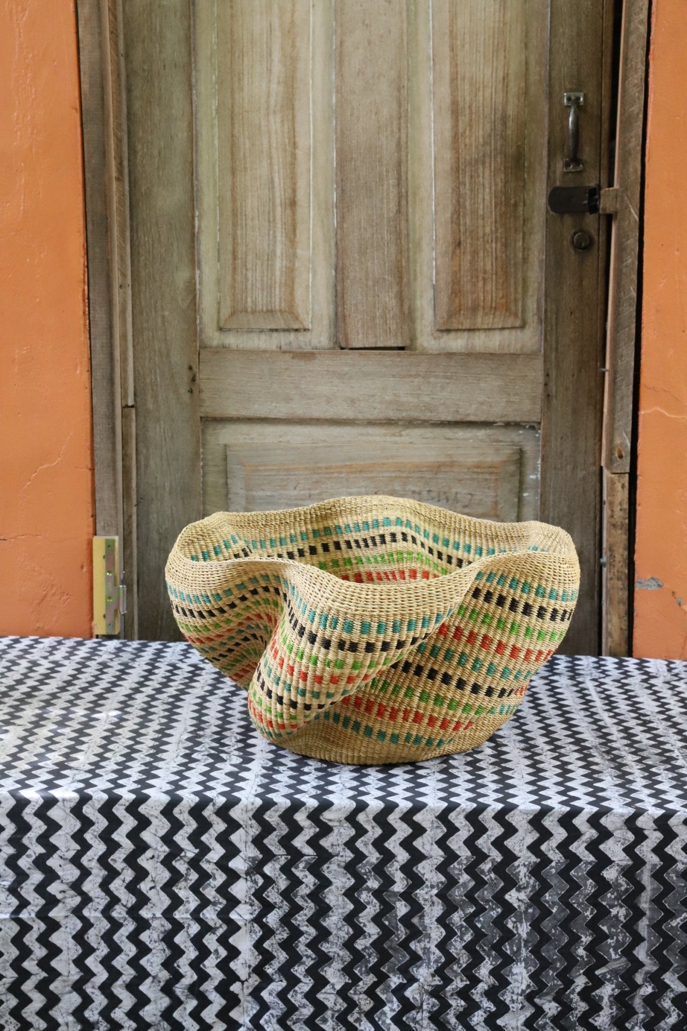 Decorative handwoven straw basket with colorful patterns on a black and white cloth against a wooden door.