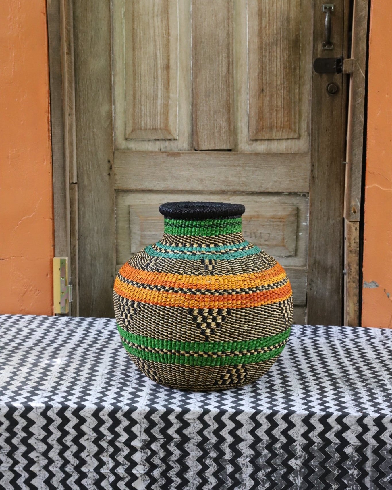 Decorative handwoven basket with colorful patterns on a black and white cloth against a wooden door.
