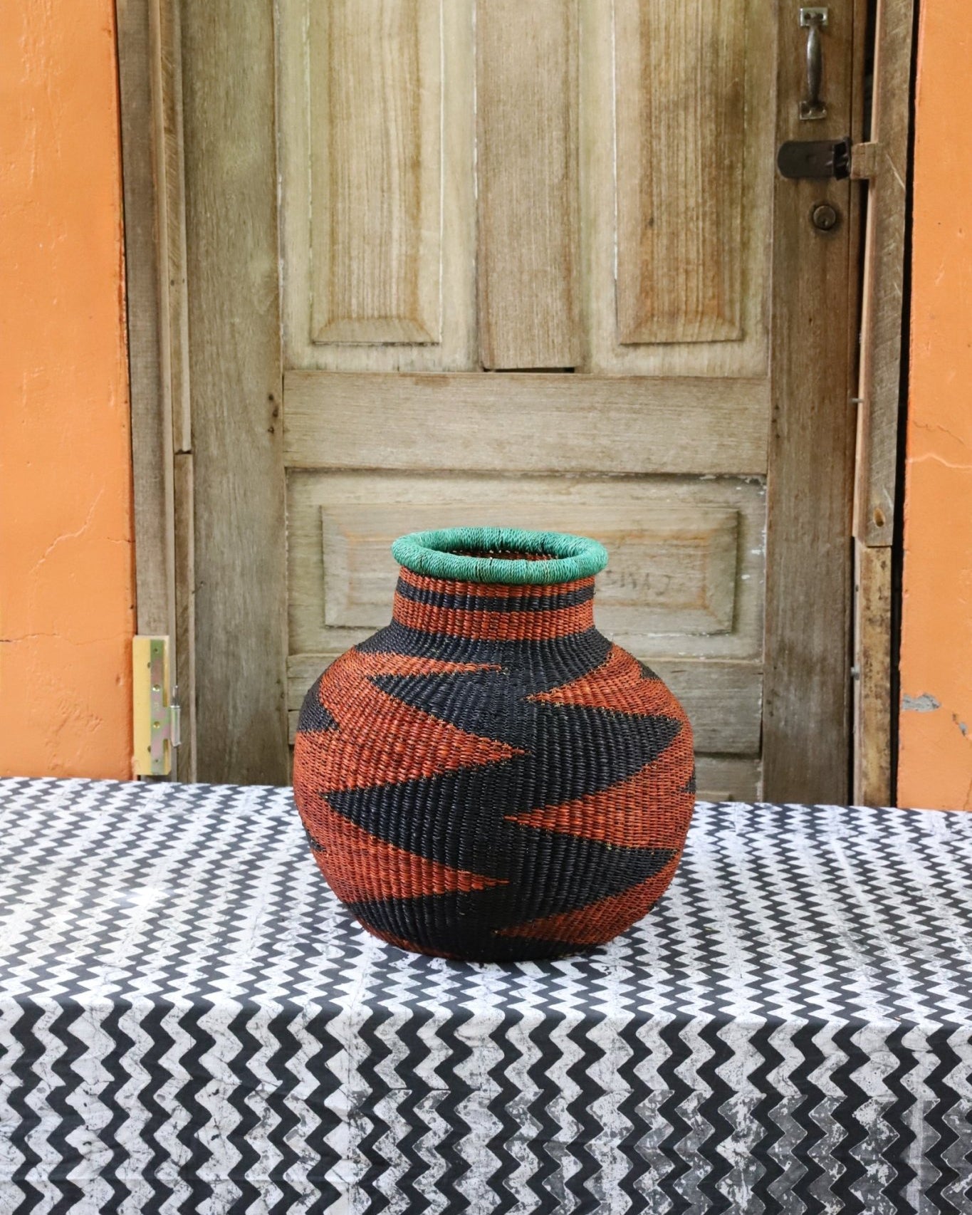 Decorative handwoven basket with colorful patterns on a black and white cloth against a wooden door.