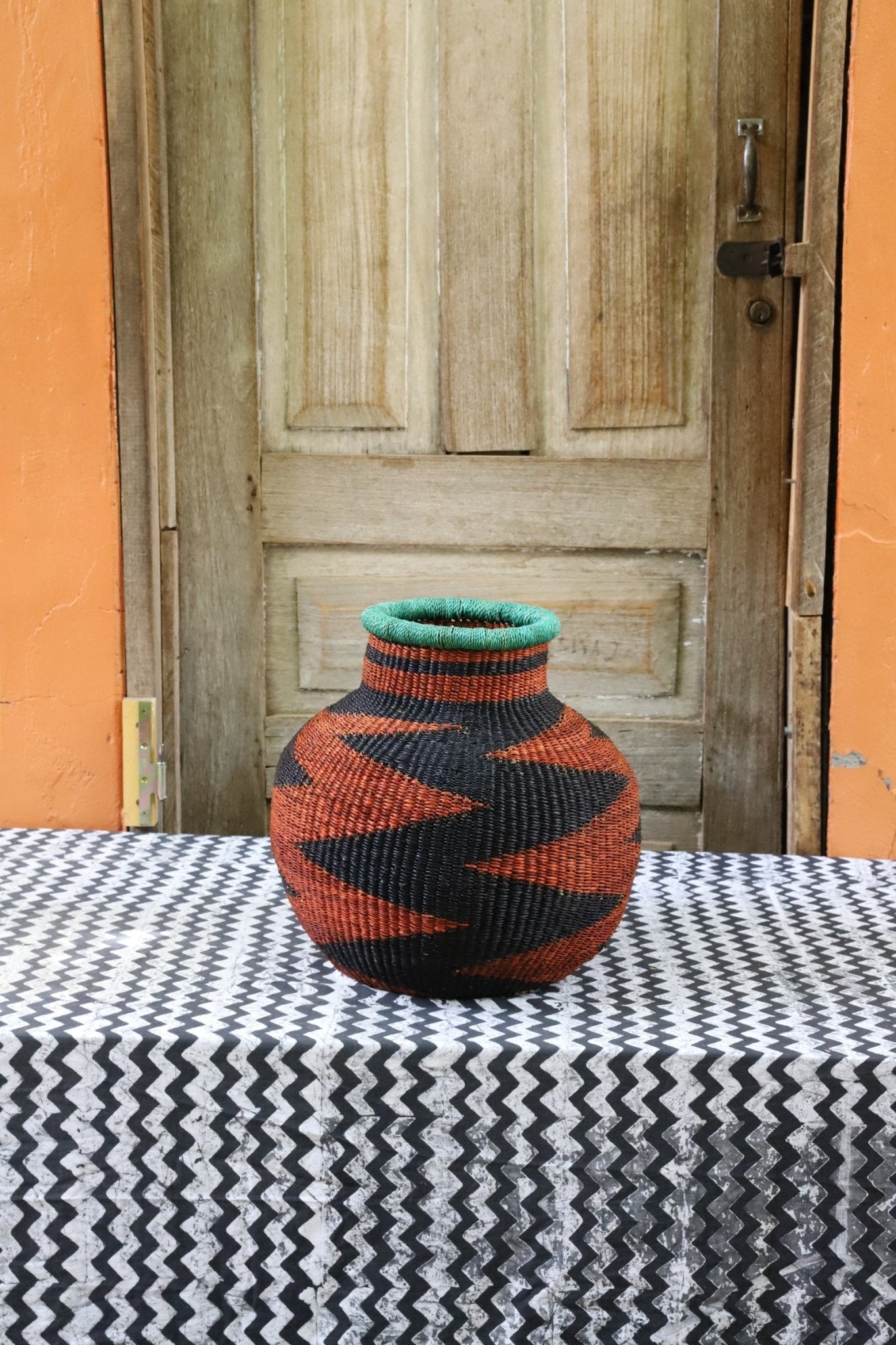 Decorative handwoven basket with colorful patterns on a black and white cloth against a wooden door.
