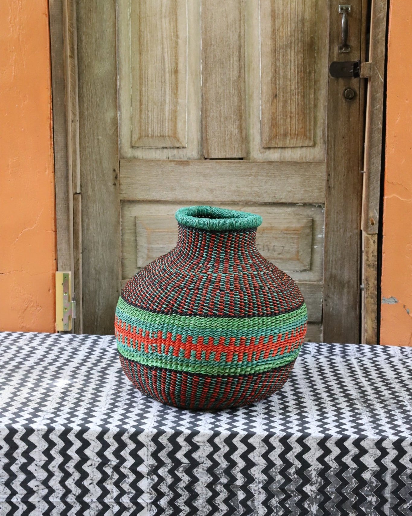 Decorative handwoven basket with colorful patterns on a black and white cloth against a wooden door.