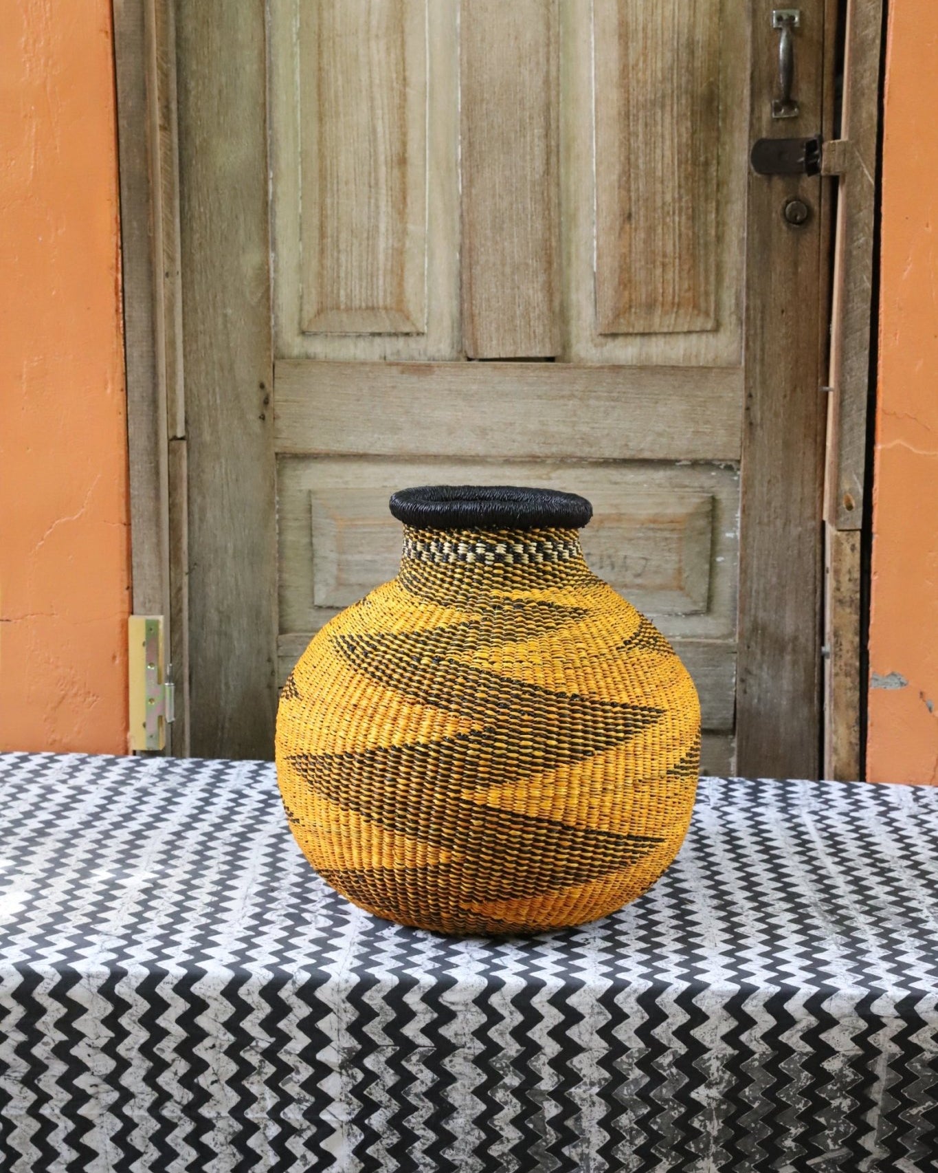 Decorative handwoven basket with colorful patterns on a black and white cloth against a wooden door.