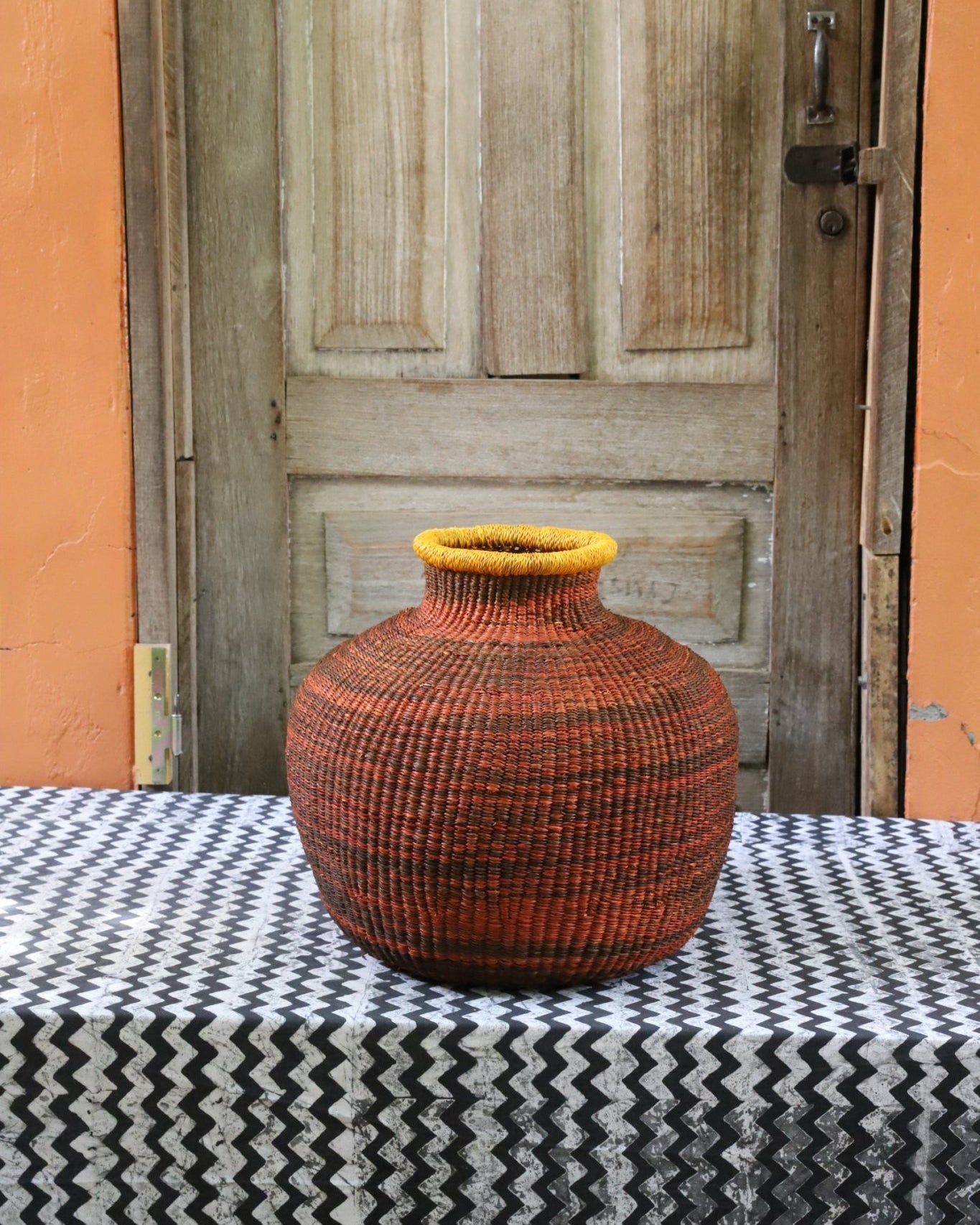 Decorative handwoven basket with colorful patterns on a black and white cloth against a wooden door.