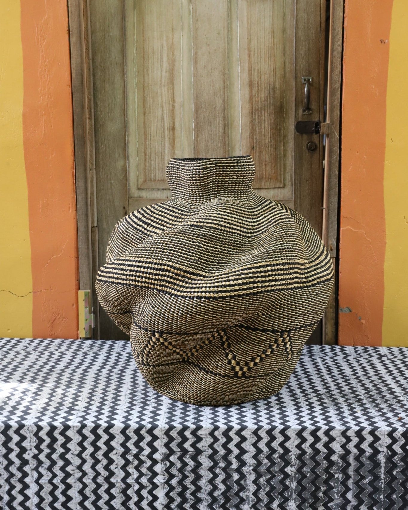 A handwoven piece with decorative curves sitting on a black and white cloth against a wooden door